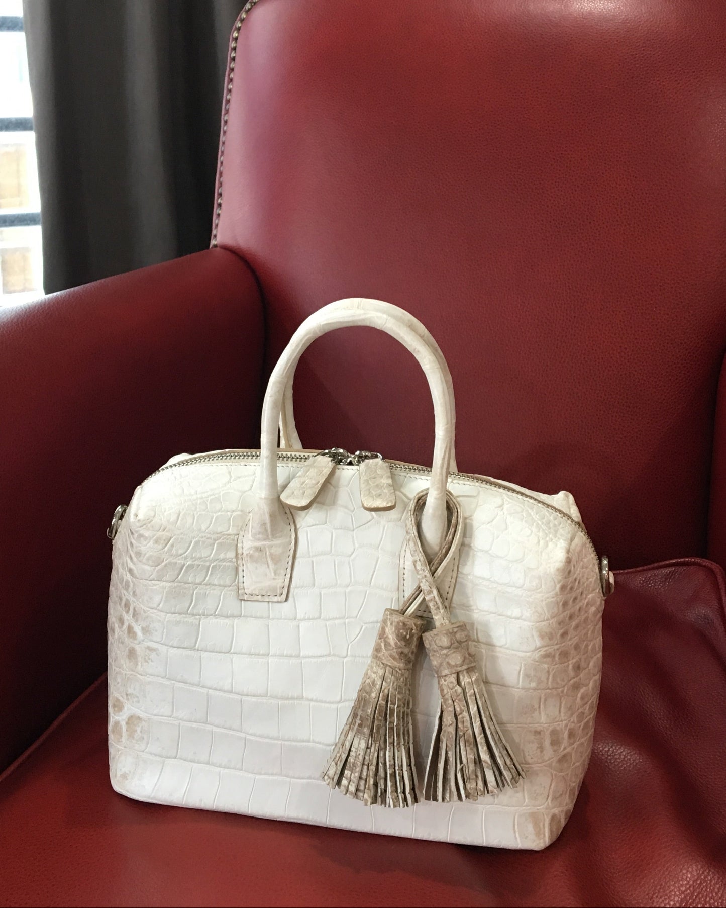White textured handbag with tassel on a red leather chair