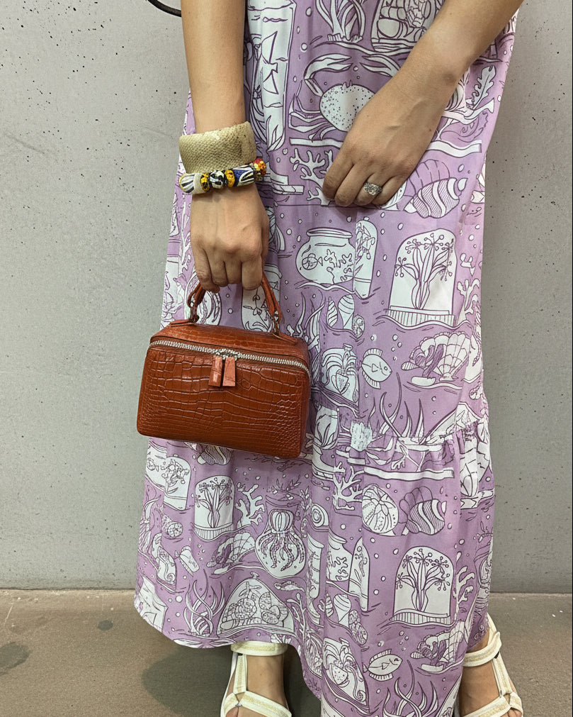 Person wearing a purple patterned dress with a colorful rug in the background.