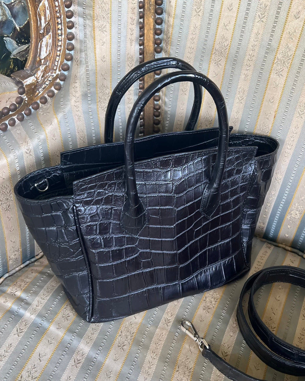 Black crocodile-patterned handbag on a striped fabric background