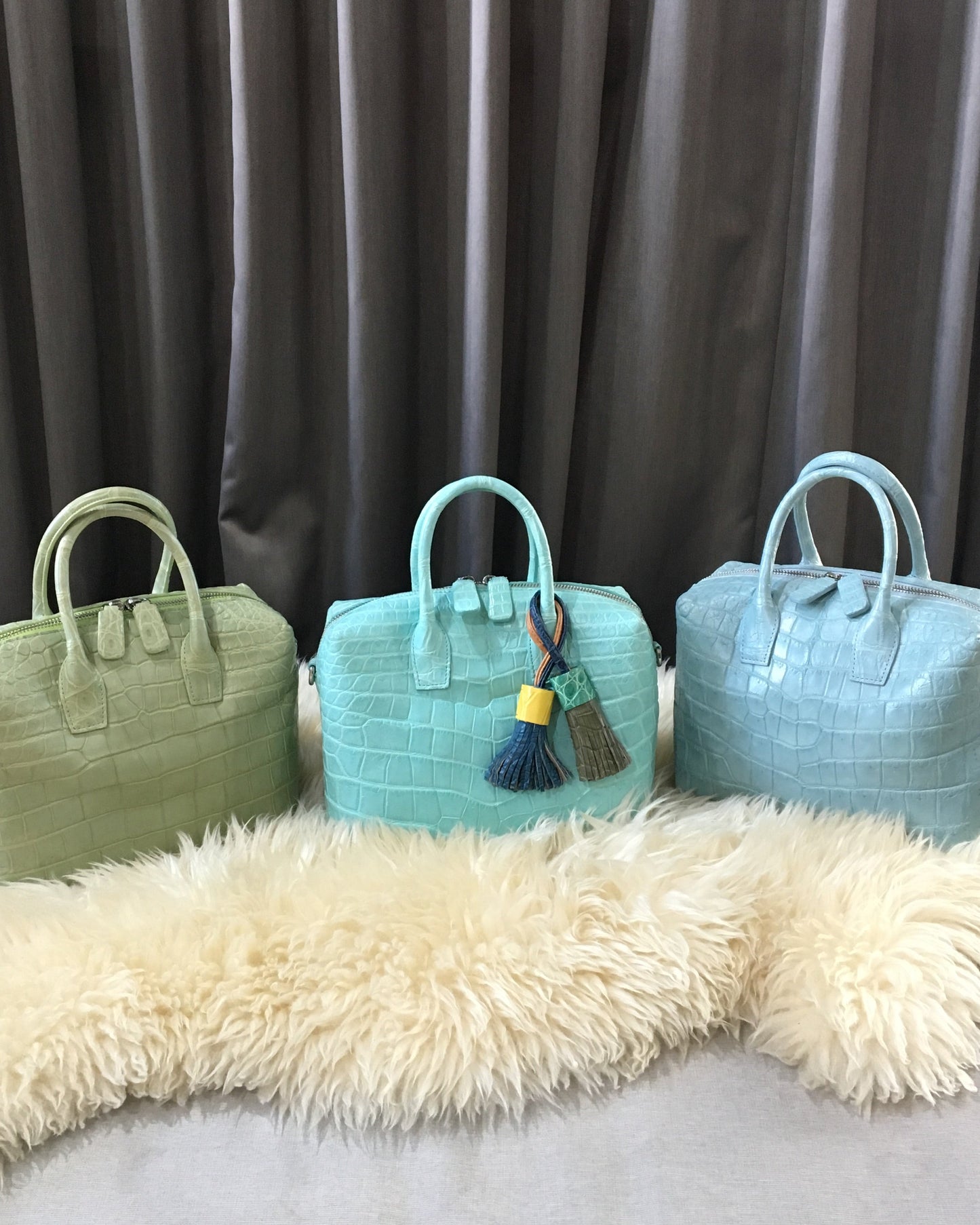 Three turquoise handbags of different sizes on a textured surface with a neutral background