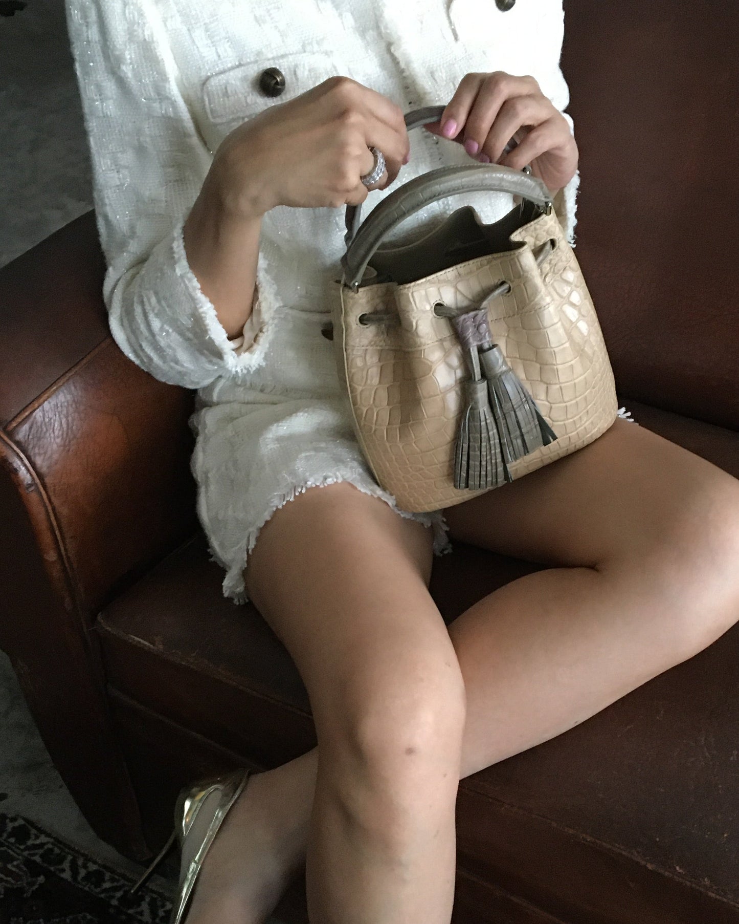 Person sitting on a brown leather chair holding a beige handbag with a tassel.