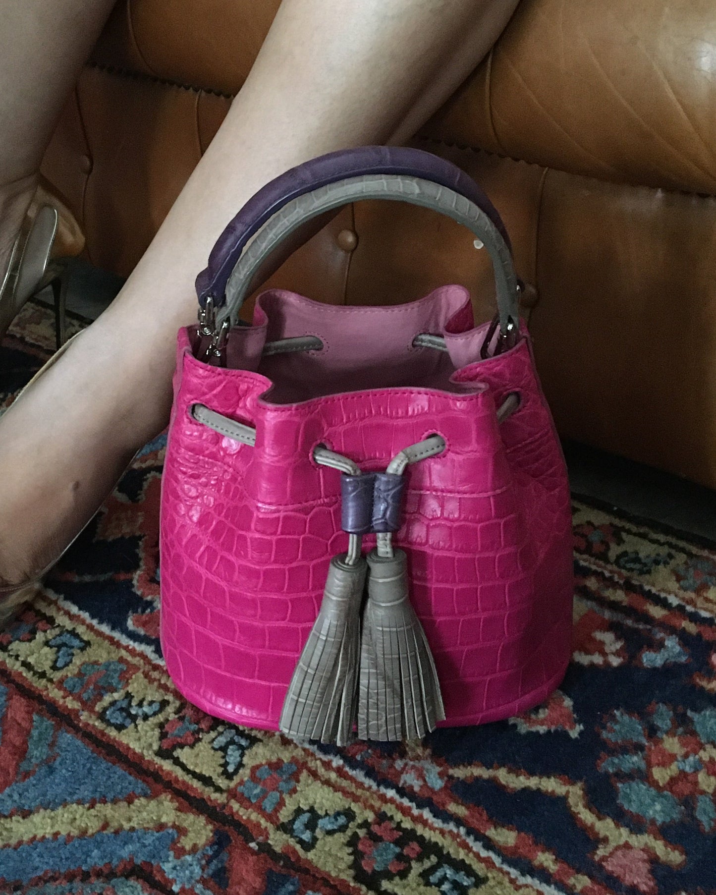 Pink handbag with a decorative tassel held by a person sitting on a brown leather couch.