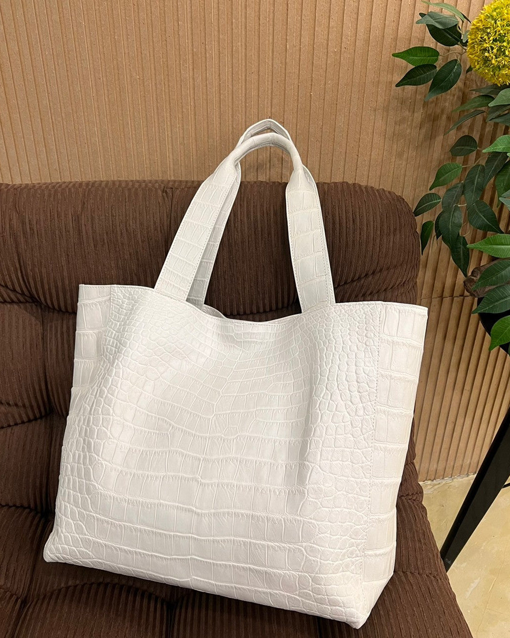 White textured tote bag on a brown couch with a plant in the background
