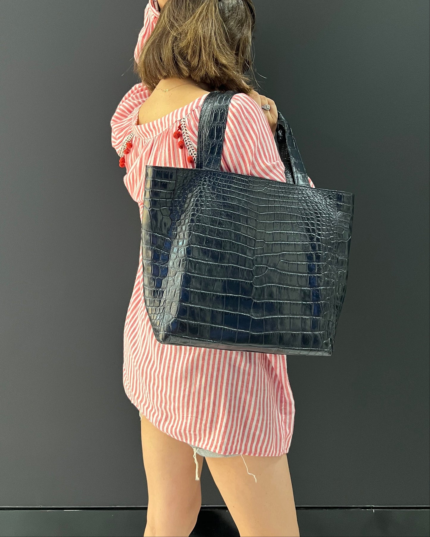 A mannequin wearing a pink and white striped dress and carrying a large black crocodile-embossed shoulder bag, shown against a dark gray background.