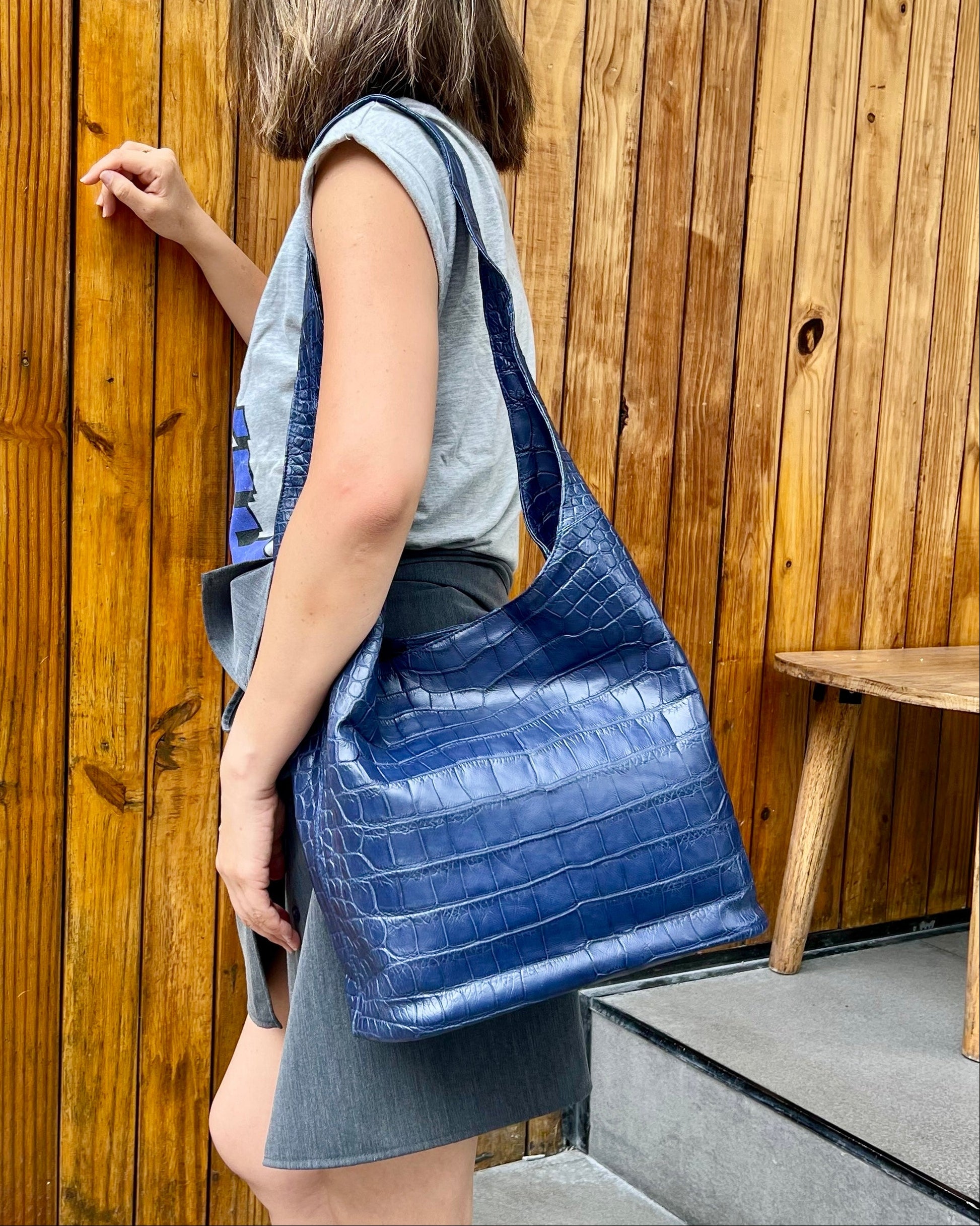Woman holding a blue textured handbag against a wooden wall.