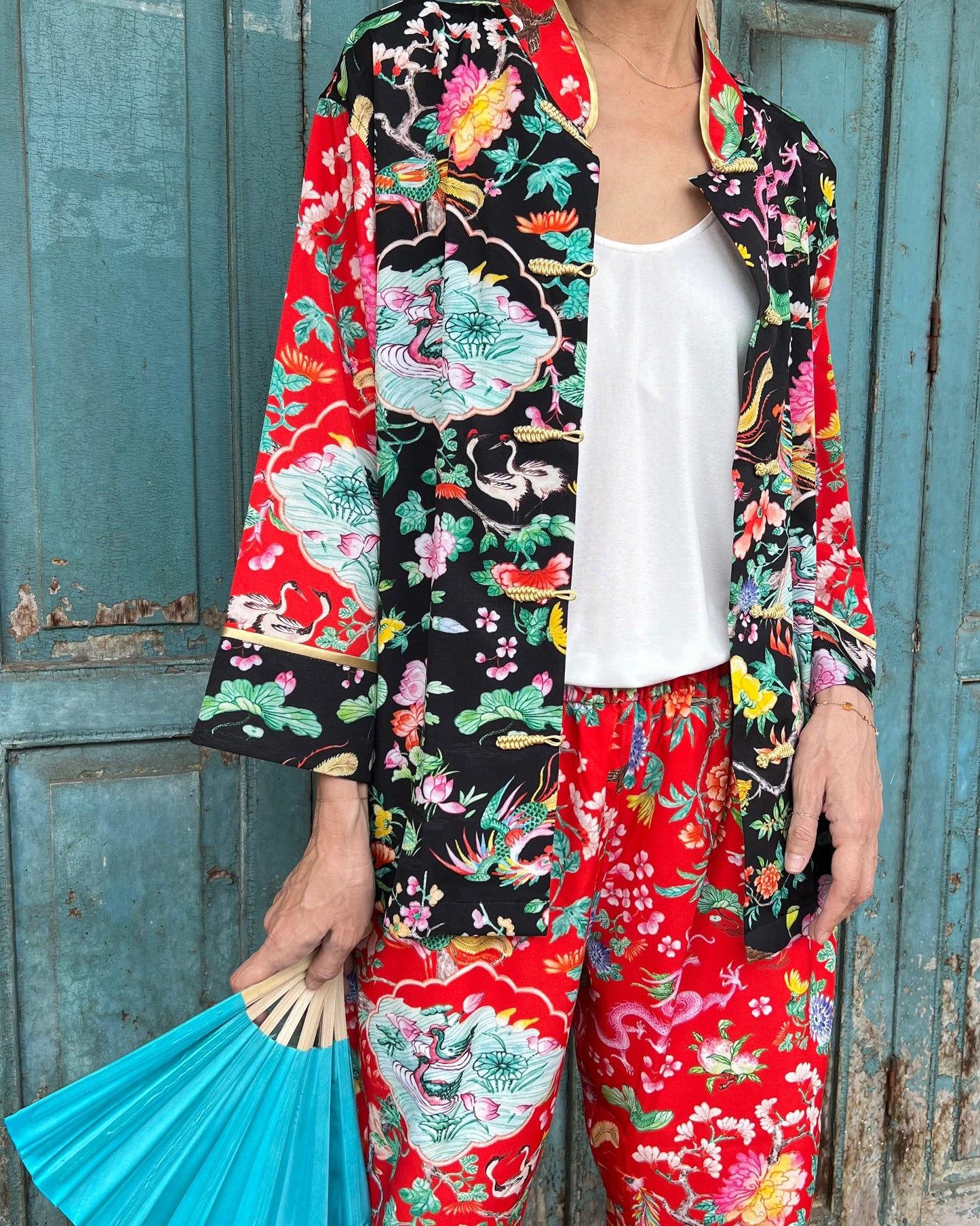 A woman wearing a black and red floral Mandarin top with a jacket and holding an umbrella.