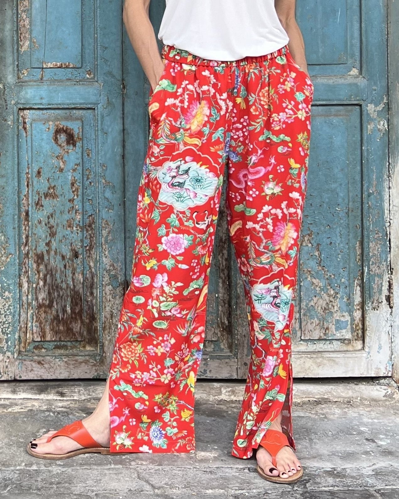 Person wearing red floral pants standing in front of a rustic blue door.