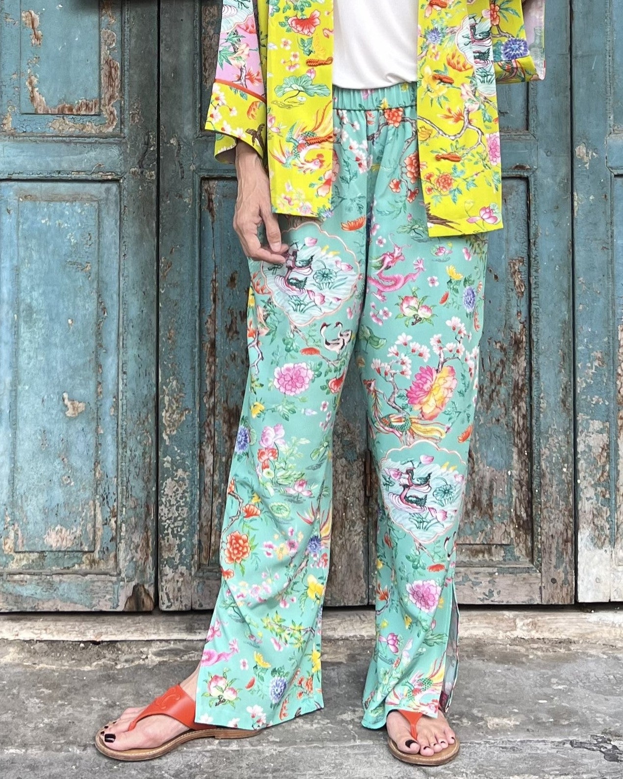 Person wearing colorful floral pants and jacket in front of a rustic wooden door.