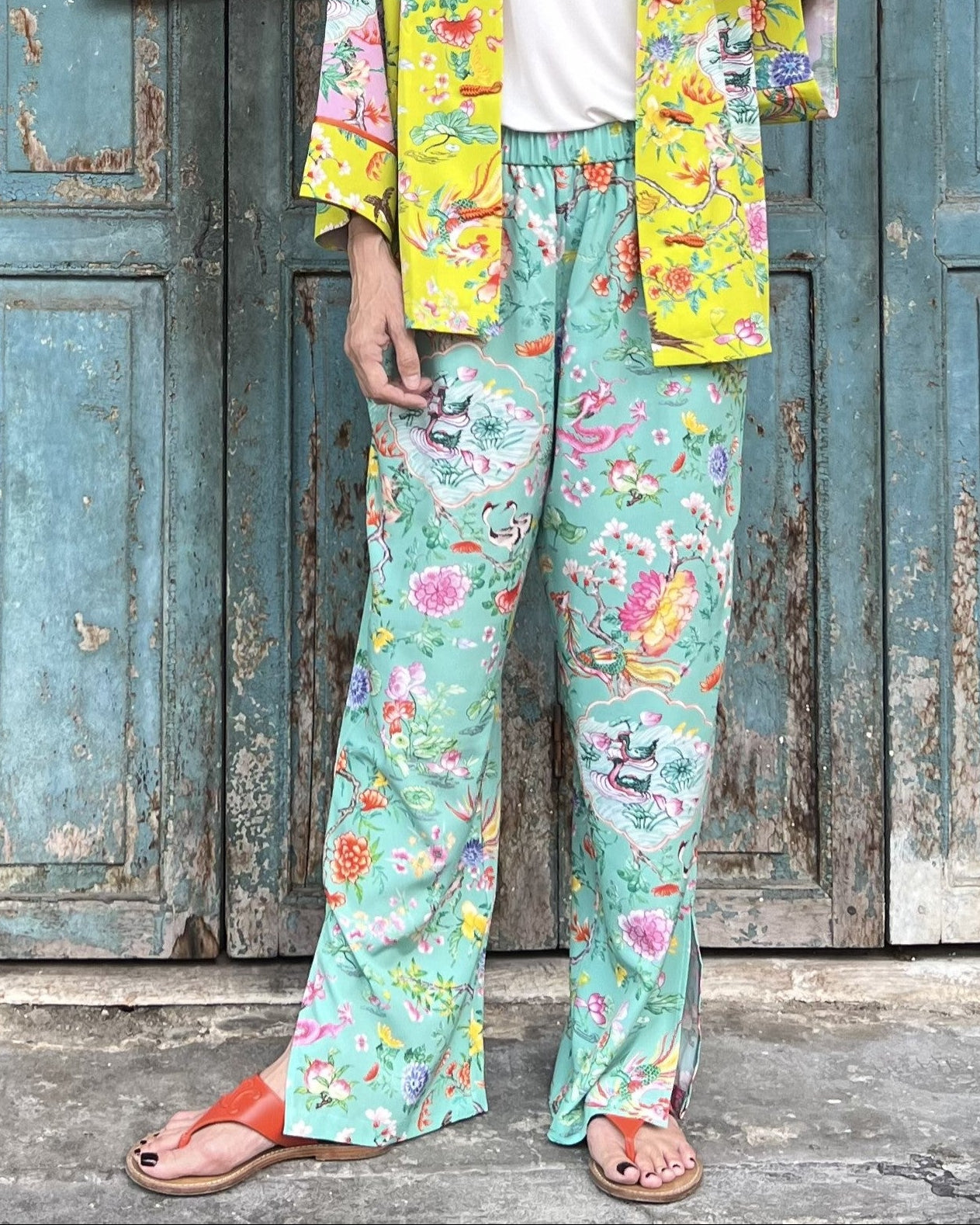 Person wearing colorful floral pants and jacket in front of a rustic wooden door.