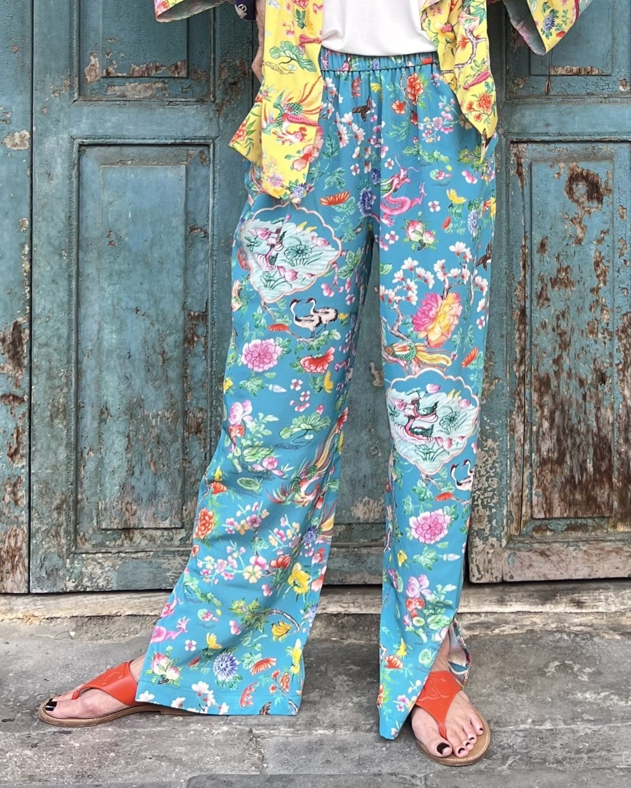 Person wearing colorful floral pants standing in front of a weathered wooden door.
