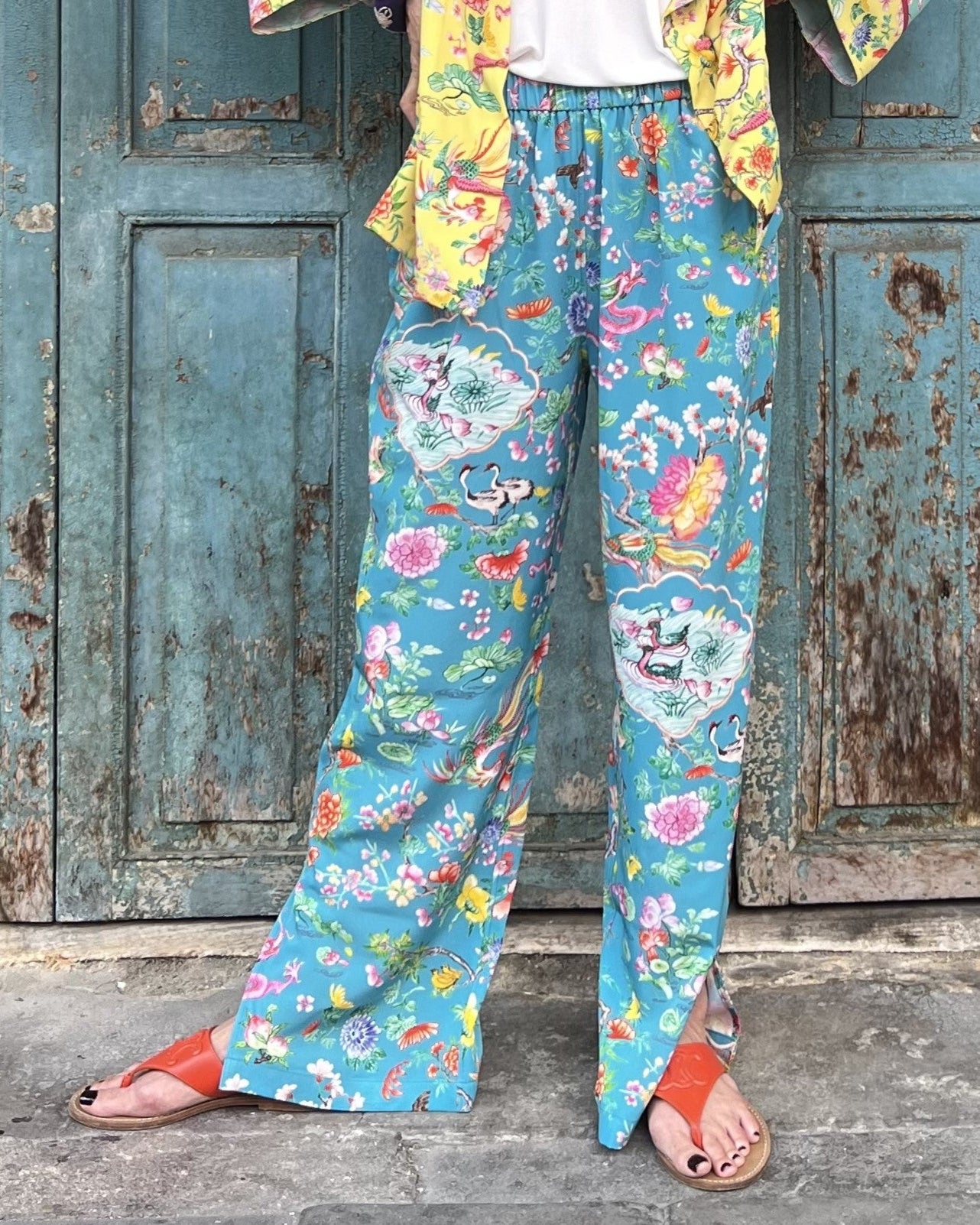 Person wearing colorful floral pants standing in front of a weathered wooden door.