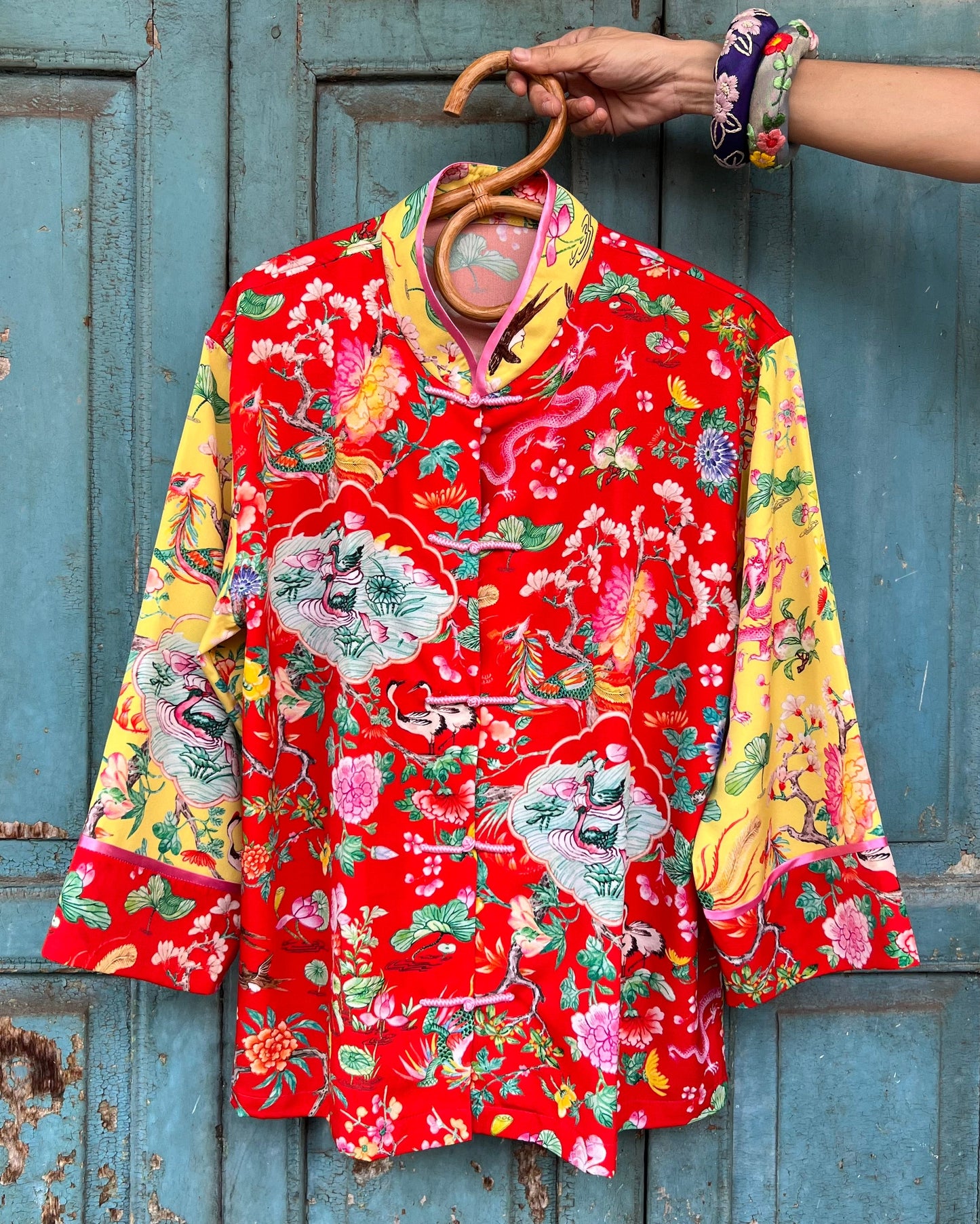 Colorful floral-patterned jacket on a hanger against a rustic blue wooden door.