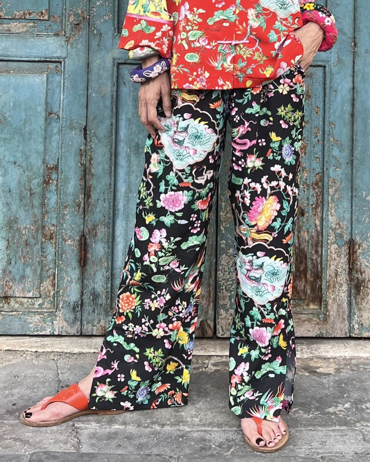 Person wearing colorful floral pants and jacket in front of a rustic wooden door.