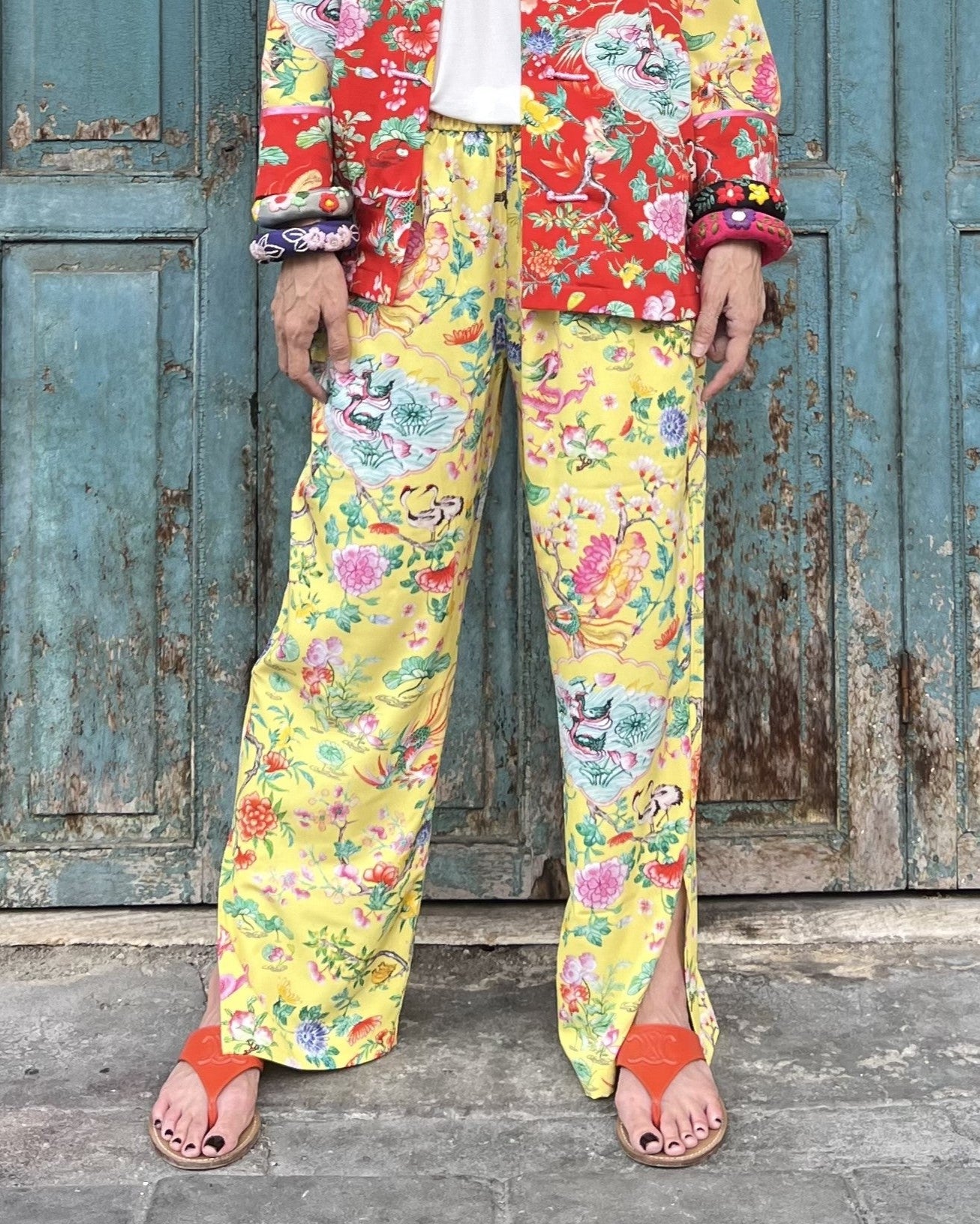 Person wearing a colorful floral outfit in front of a rustic wooden door.