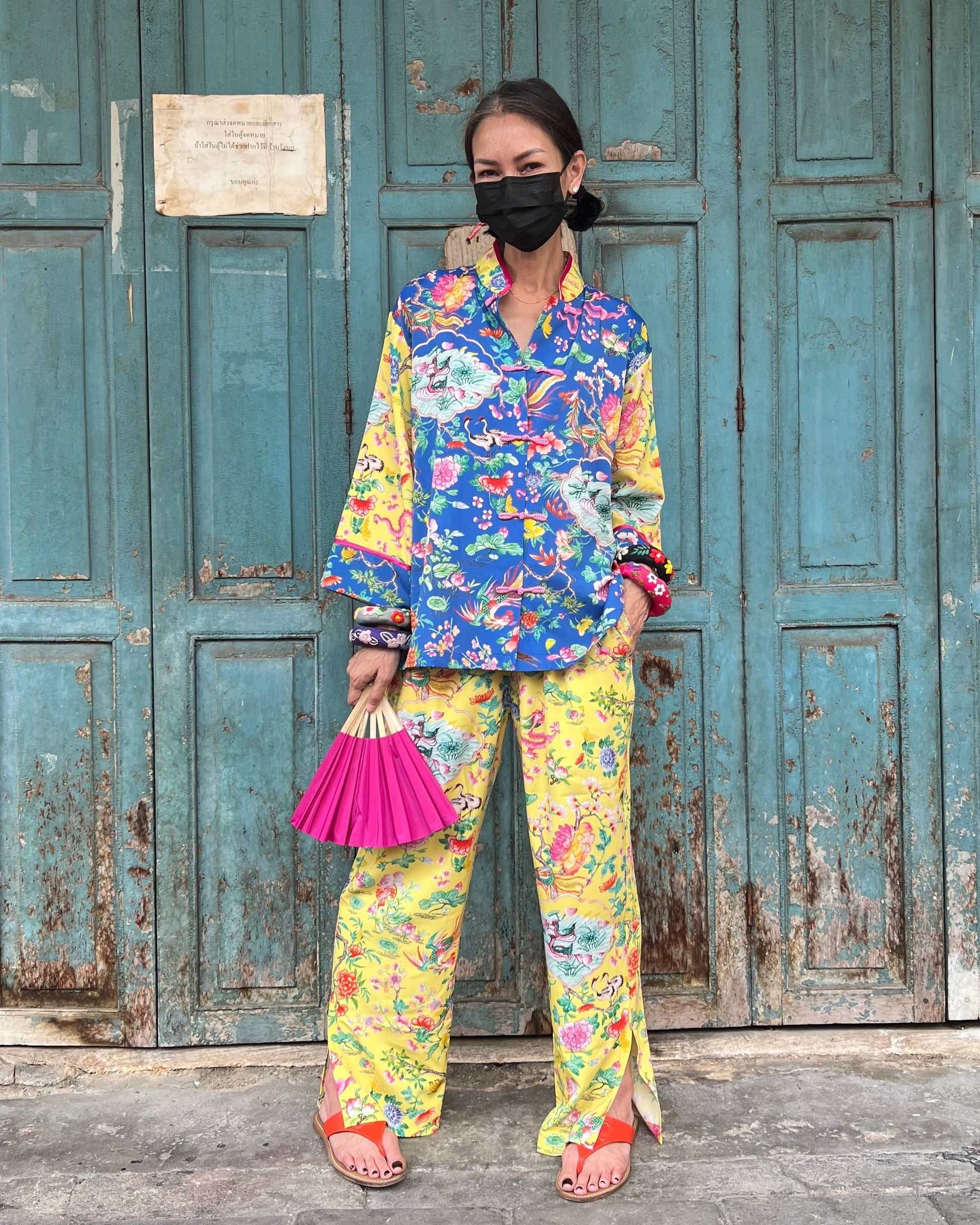 Person wearing a colorful outfit with a floral pattern in front of a weathered blue door.