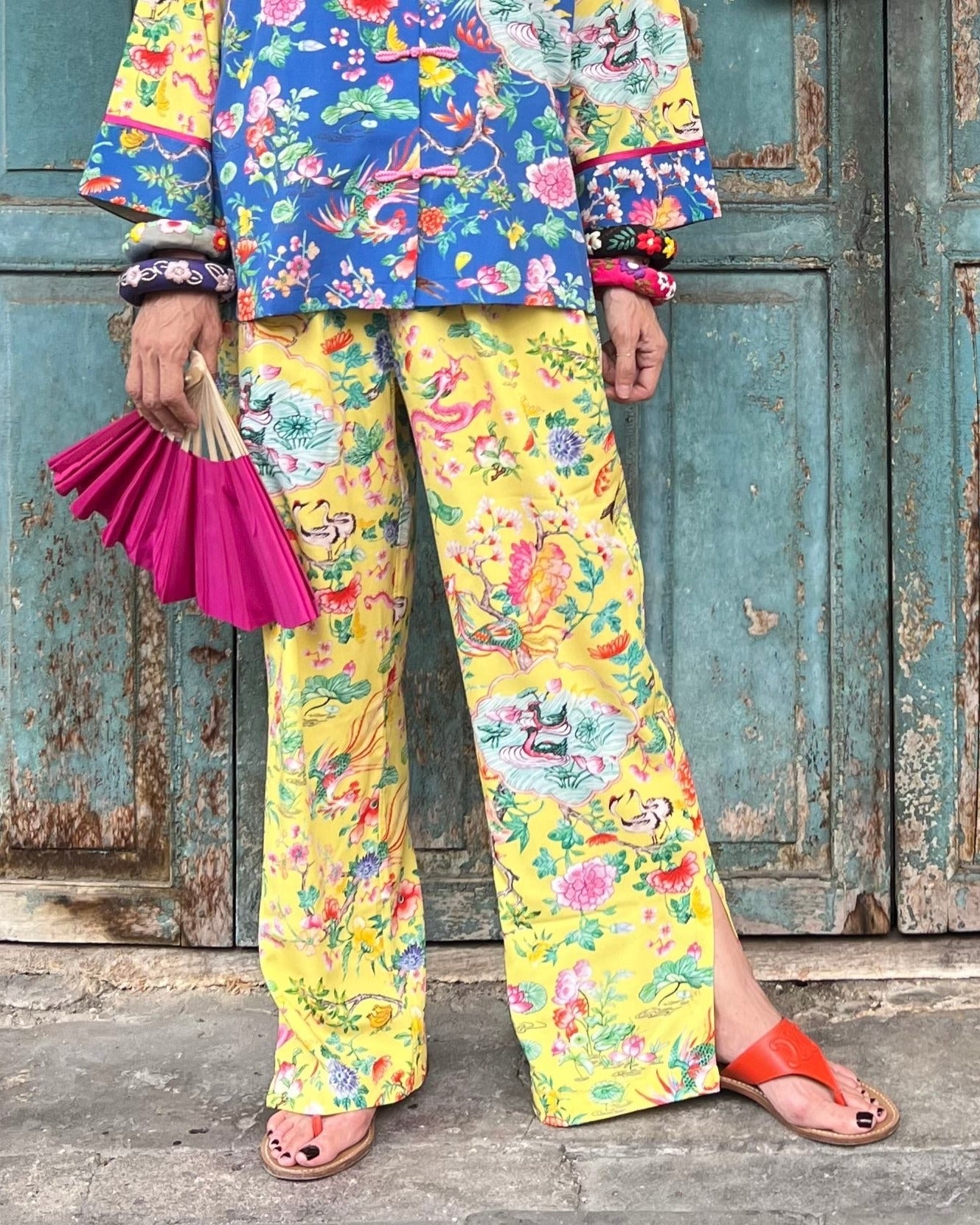 A pair of yellow pants with hand-drawn floral prints and red accents, displayed against a blue background.