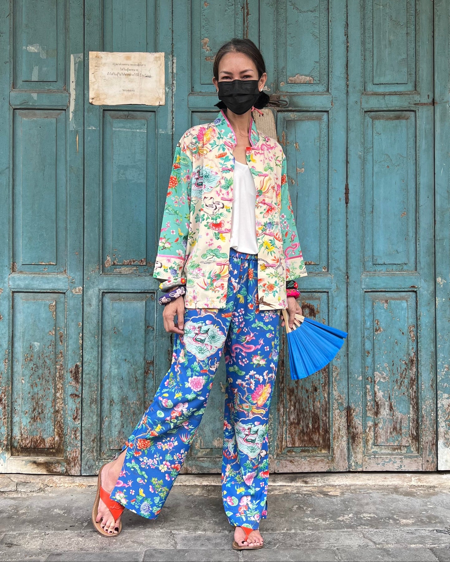 Woman in colorful floral outfit standing in front of a rustic door.