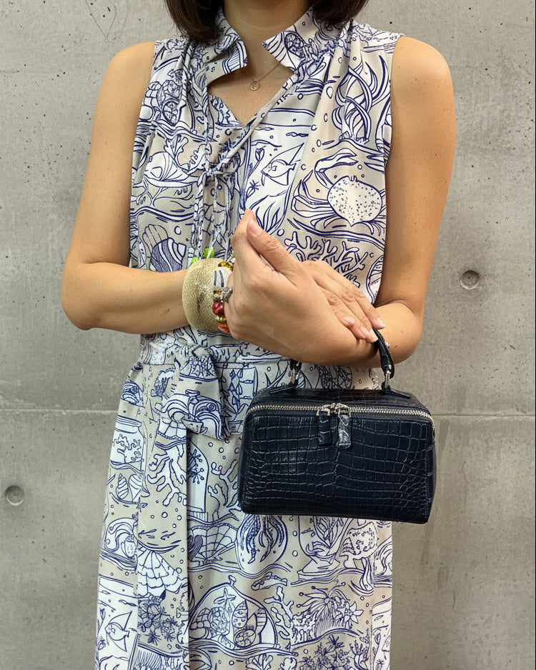Person holding a black handbag with a patterned dress and colorful bracelet.