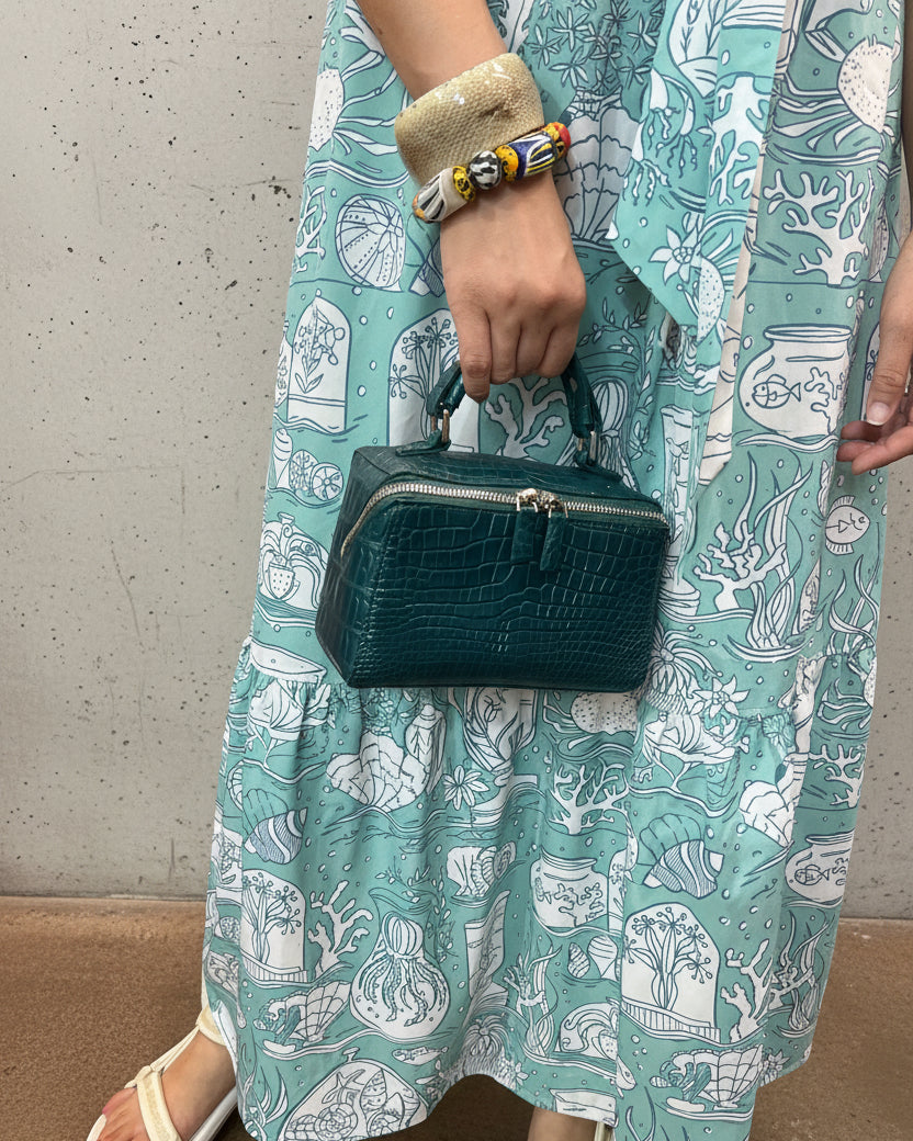 Person holding a green clutch bag on a patterned fabric surface