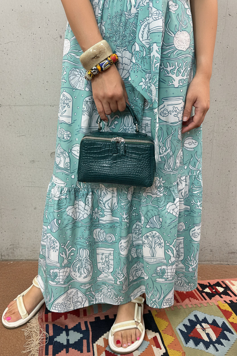 Person holding a dark green wallet on a patterned fabric surface with a colorful rug in the background.