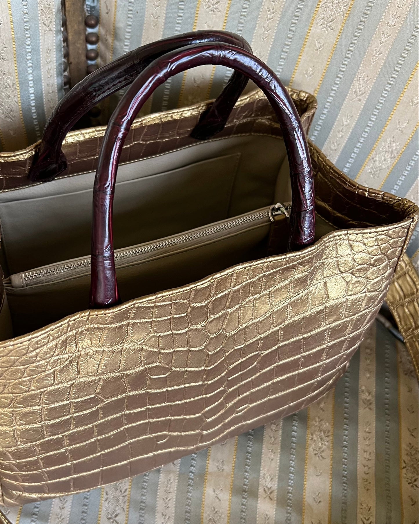Gold crocodile-patterned handbag with a brown handle on a striped fabric background