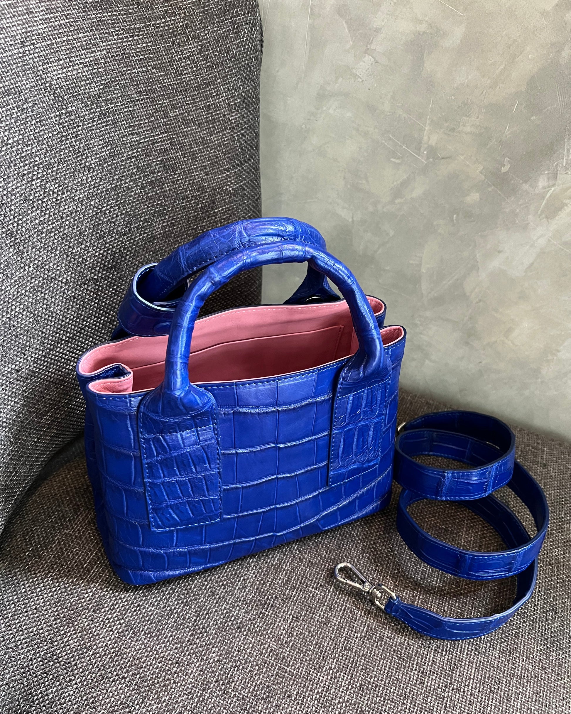 Blue textured handbag with a pink interior on a gray surface