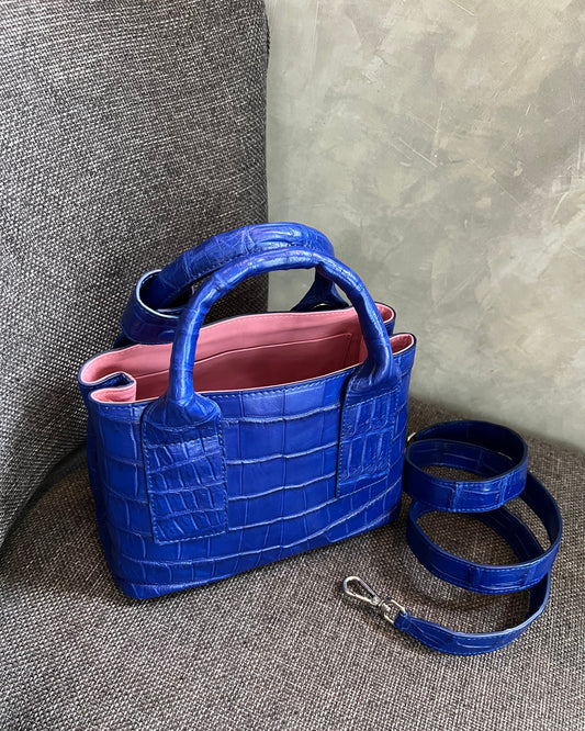 Blue textured handbag with a pink interior on a gray surface