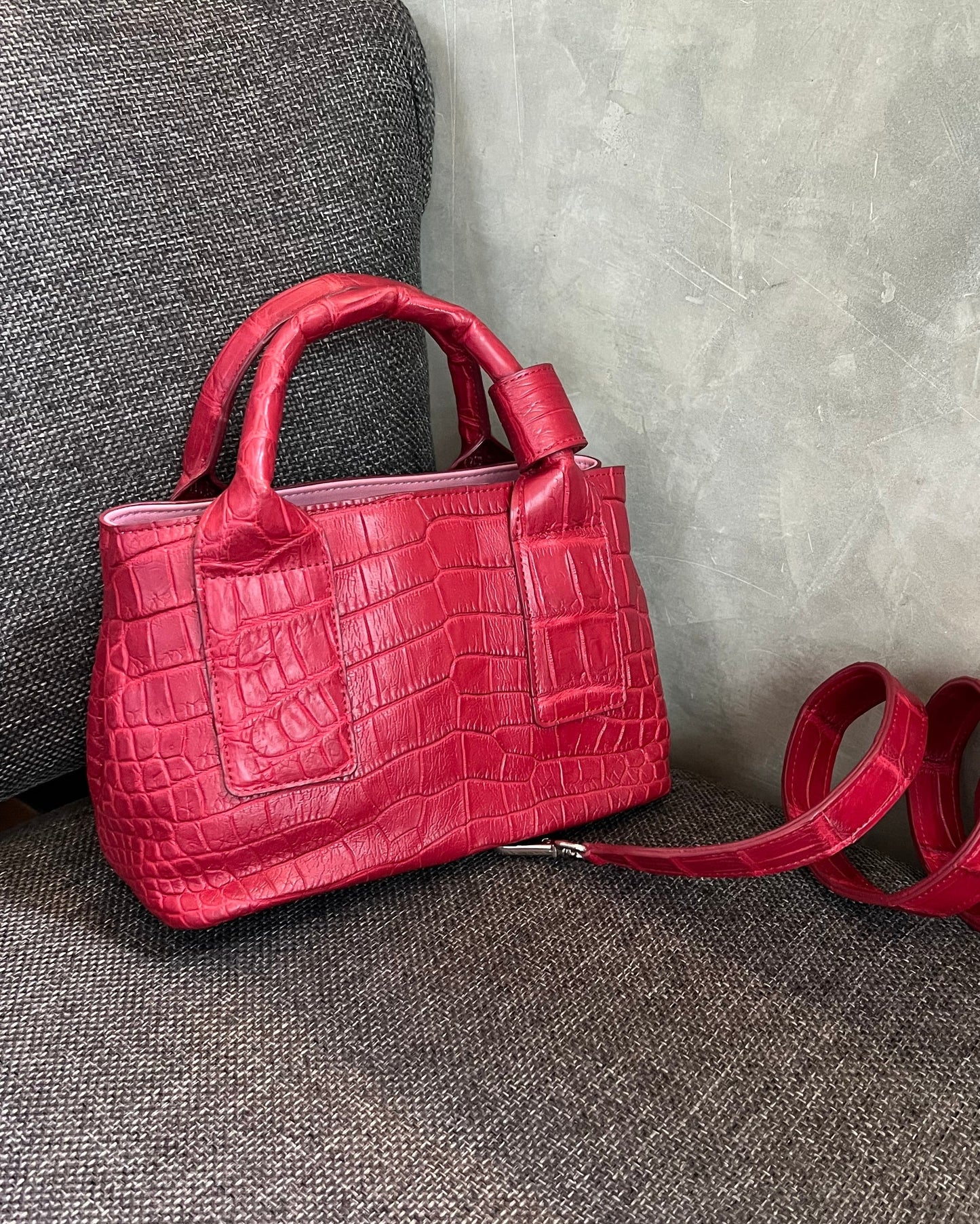 A red crocodile leather top handle bag with a pink interior lining, displayed against a grey background.