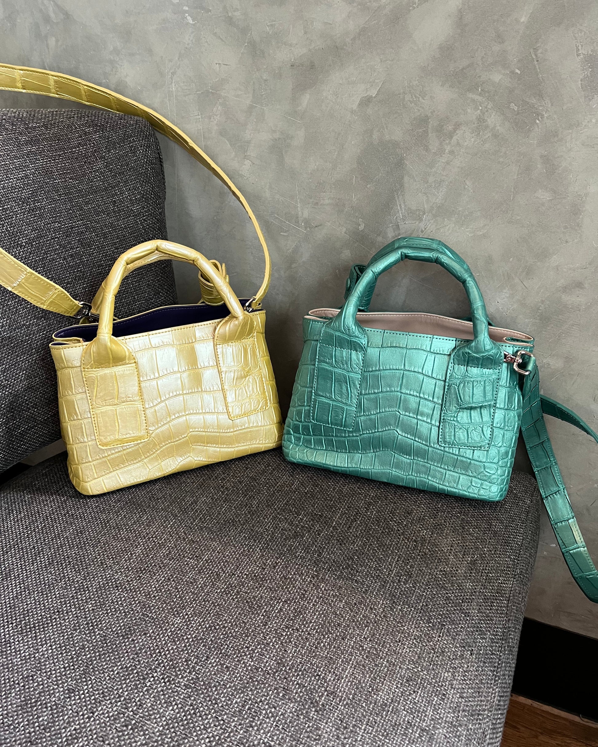 Two handbags, one green and one yellow, on a gray surface.