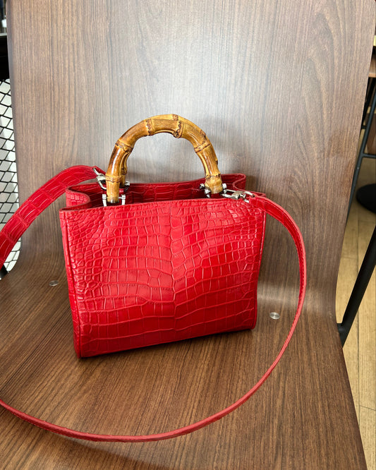 Red crocodile skin handbag with gold handle on a wooden surface