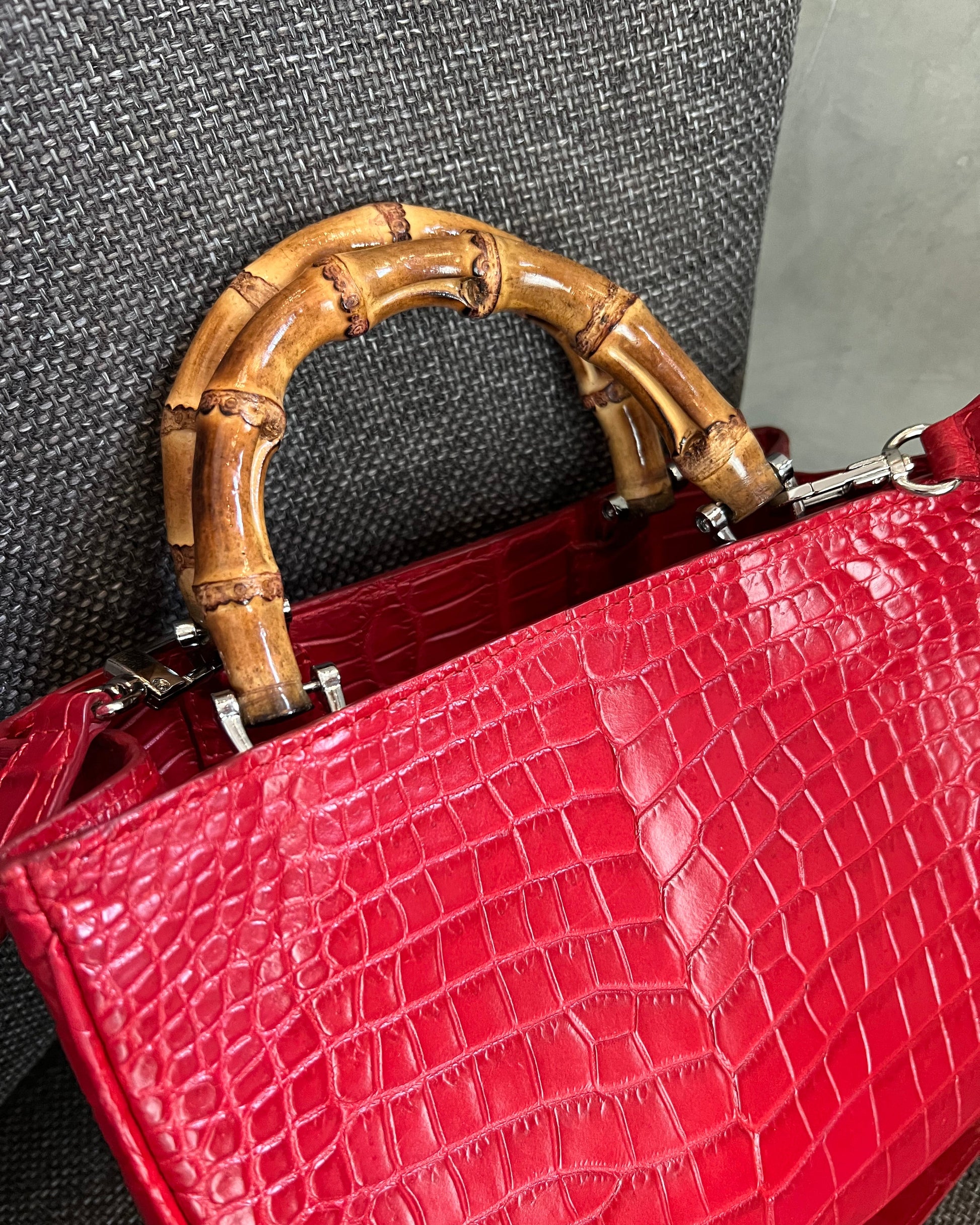 Red textured handbag with a bamboo handle on a gray surface