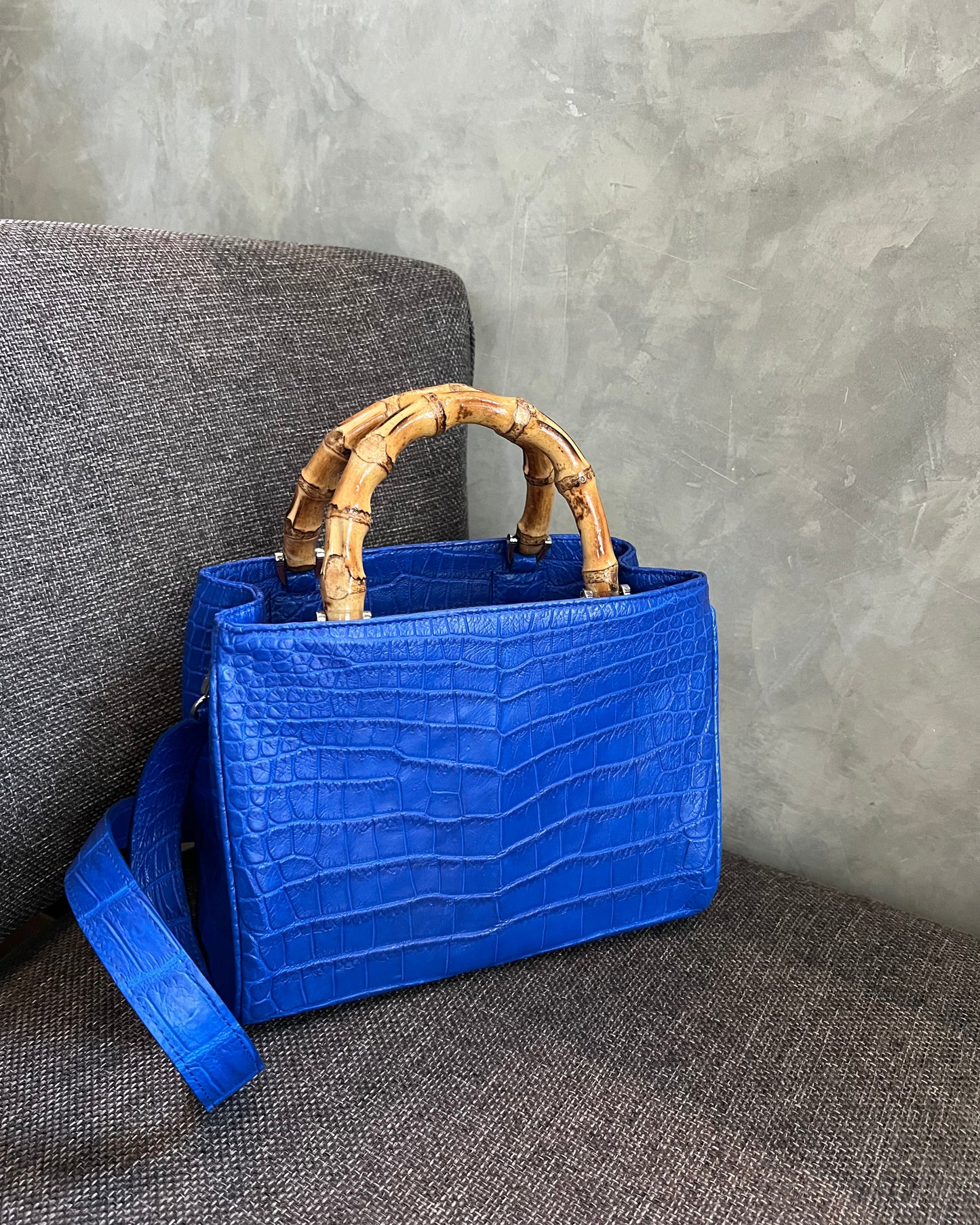 Blue handbag with bamboo handle on a gray surface