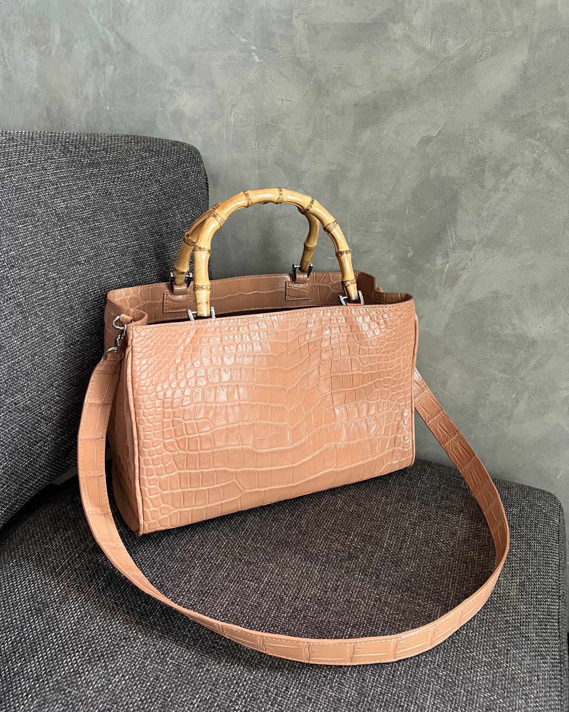 Brown leather handbag with bamboo handle on a gray textured surface