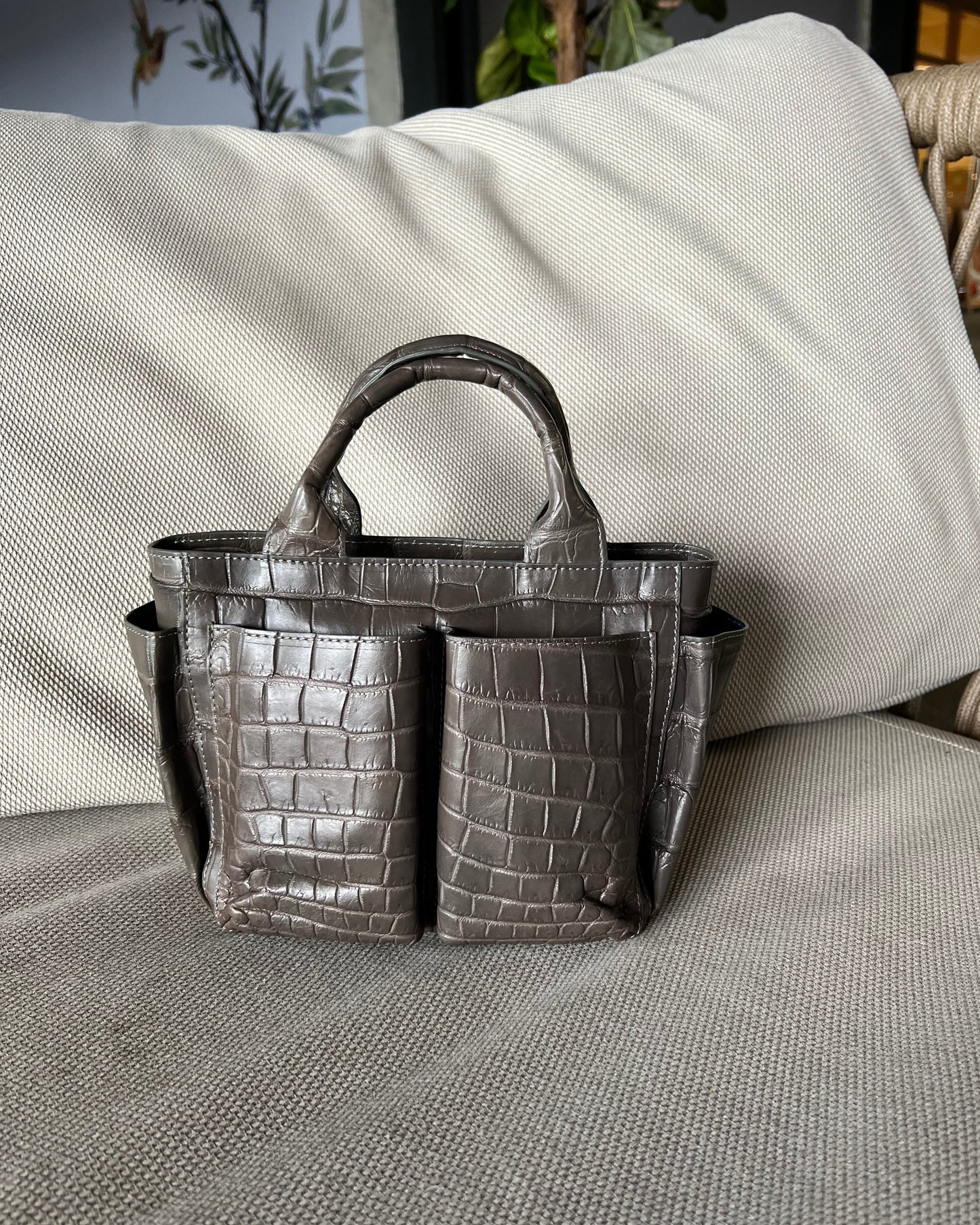 Silver crocodile-patterned handbag on a textured surface