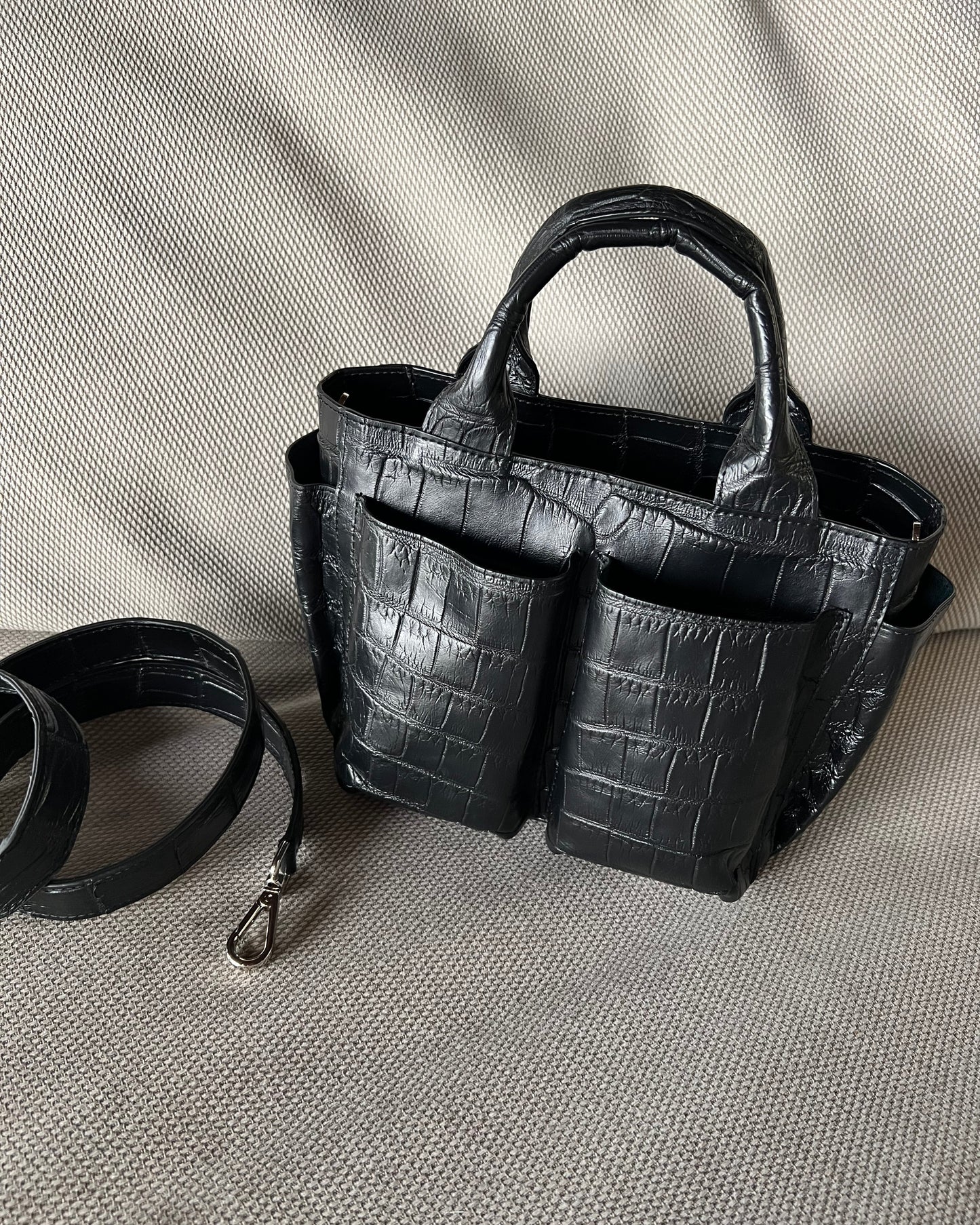 Black crocodile-patterned handbag with a detachable strap on a light gray background