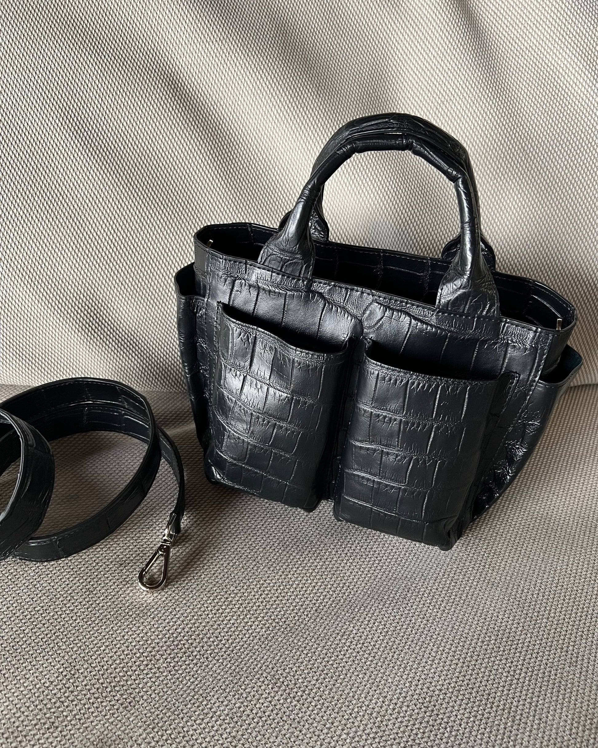 Black crocodile-patterned handbag with a detachable strap on a light gray background