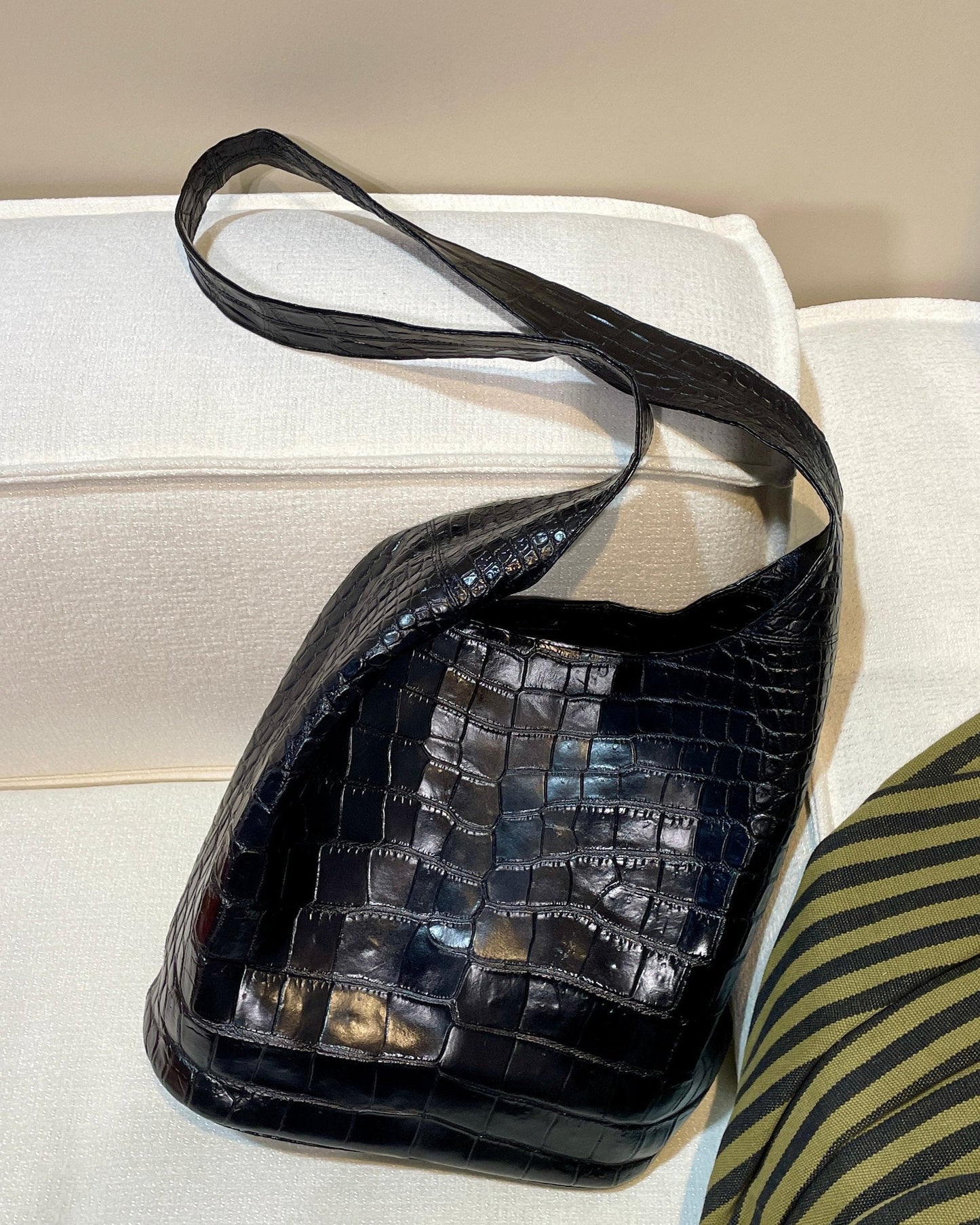 Black crocodile-patterned handbag on a light-colored surface