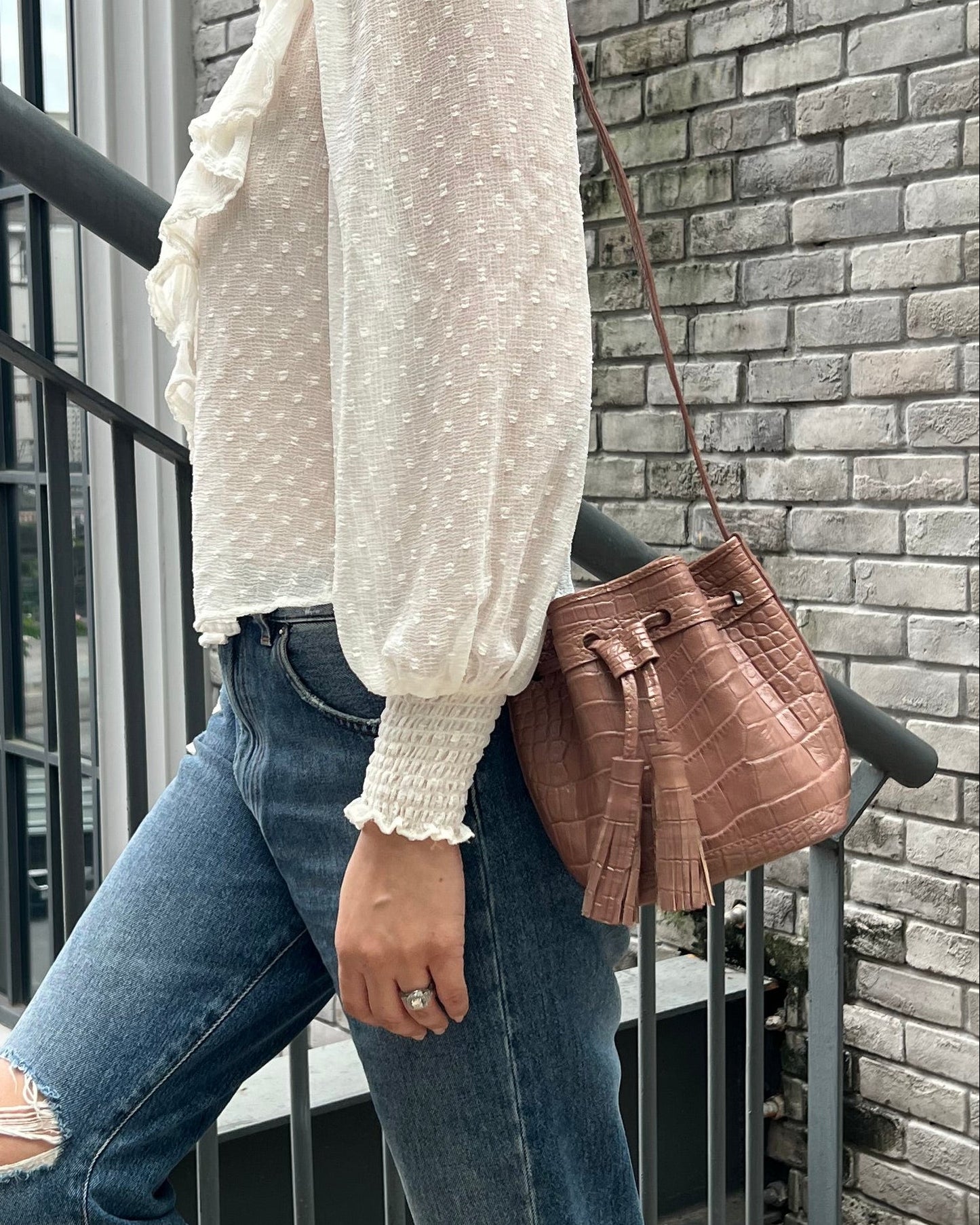 A woman wearing a white textured knit sweater, distressed blue jeans, and brown boots, carrying a brown leather shoulder bag while walking down outdoor stone steps.