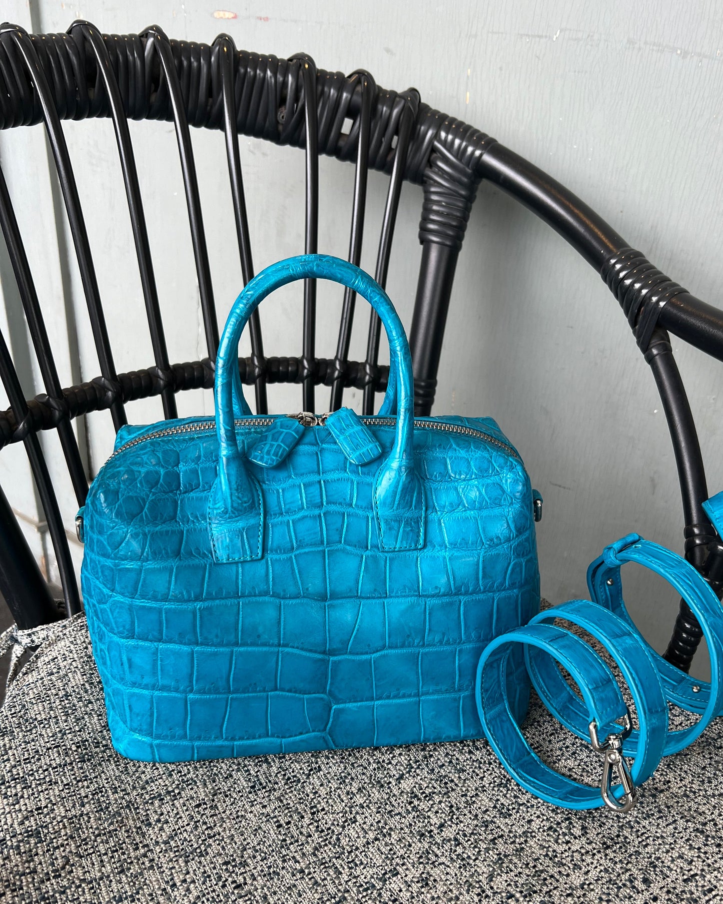 Blue handbag with a textured pattern on a black wicker chair.