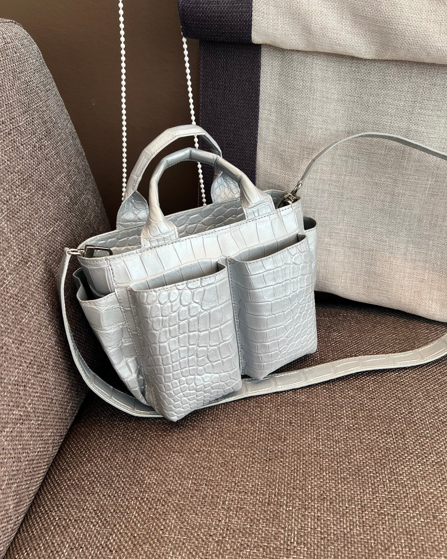 Gray crocodile-patterned handbag on a brown couch