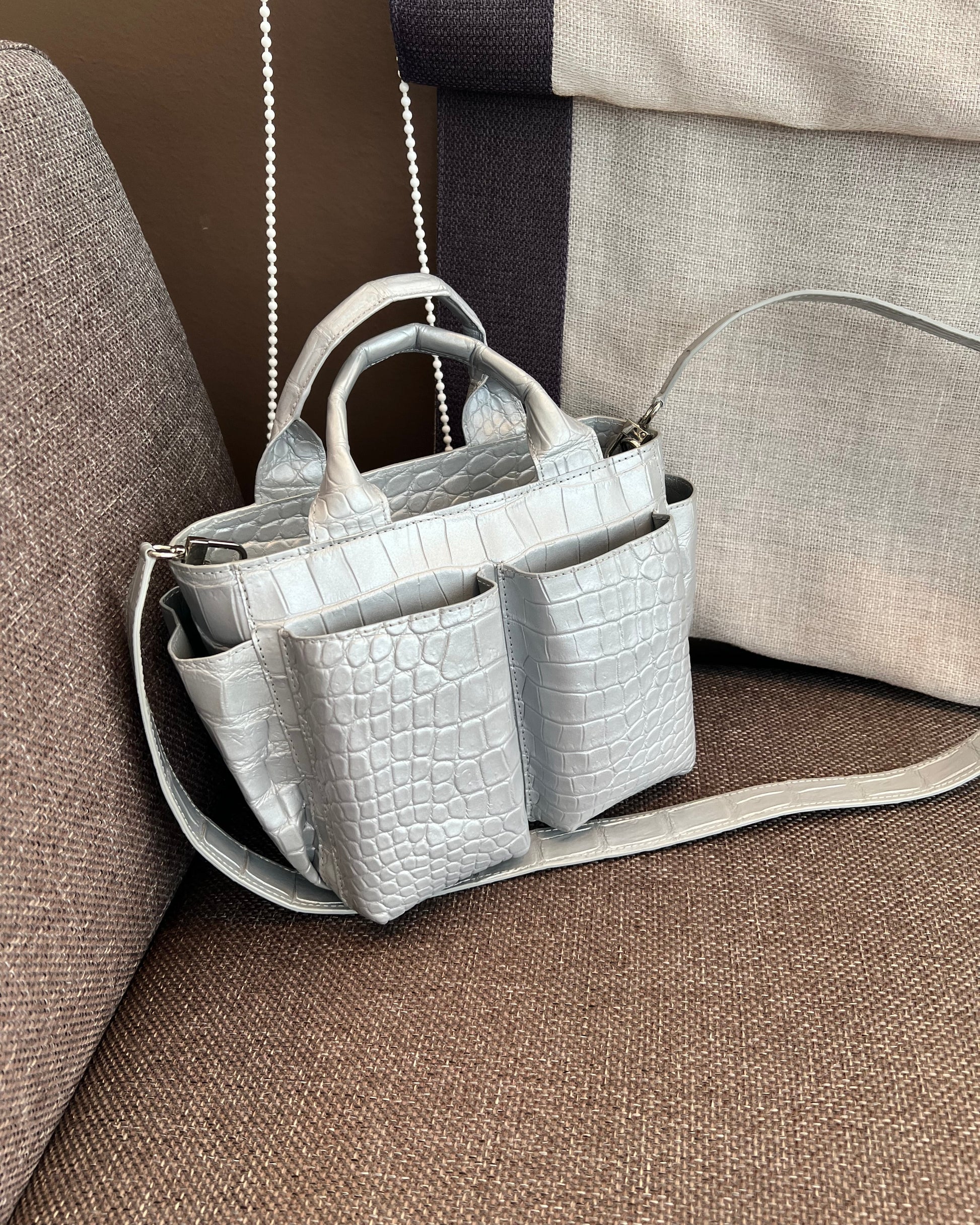 Gray crocodile-patterned handbag on a brown couch