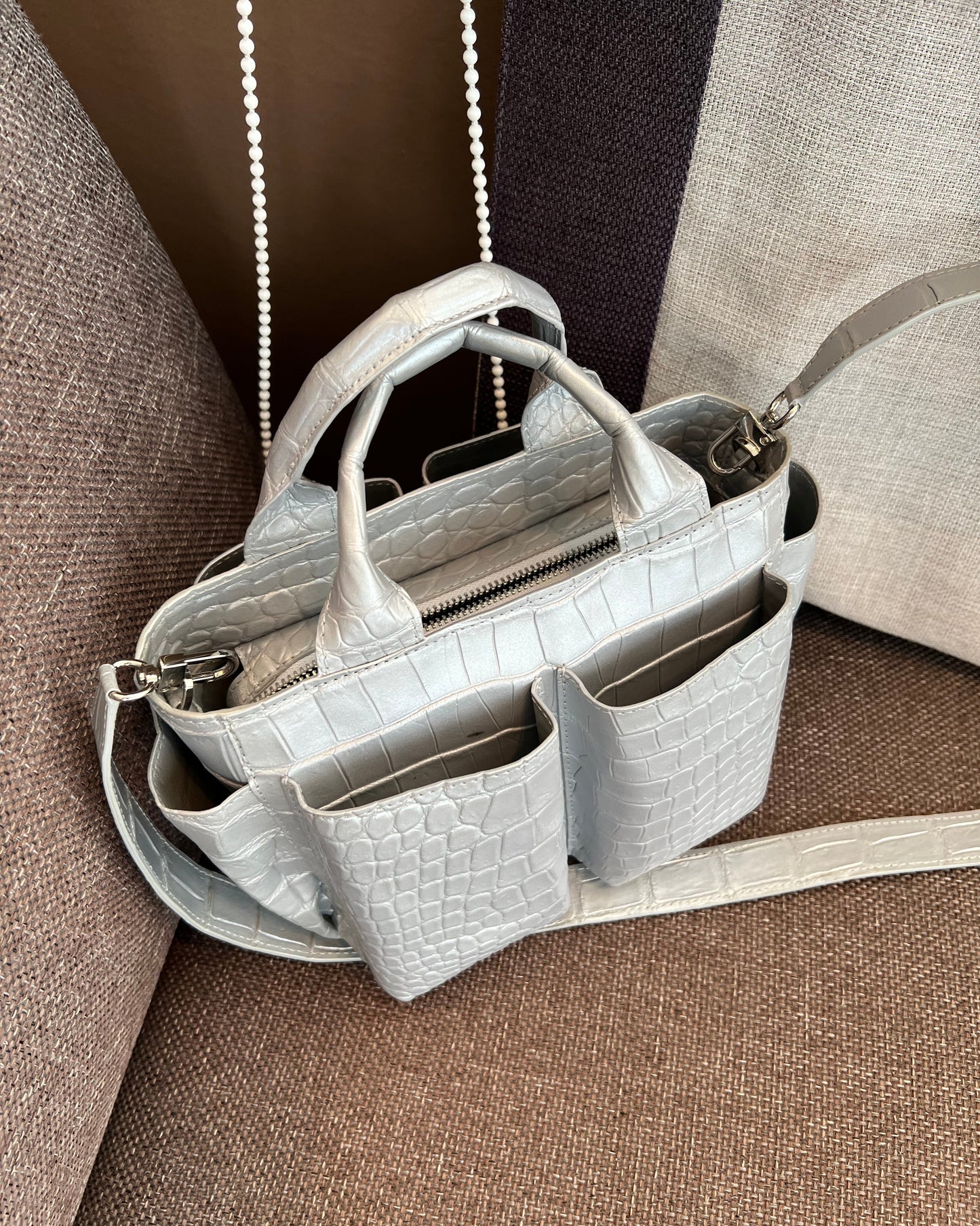 Light gray handbag with crocodile texture on a brown textured surface