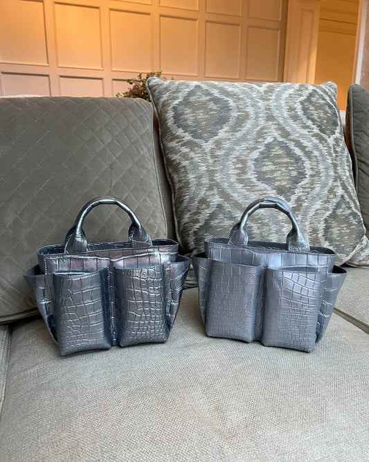Two gray handbags on a textured surface with a patterned cushion in the background.