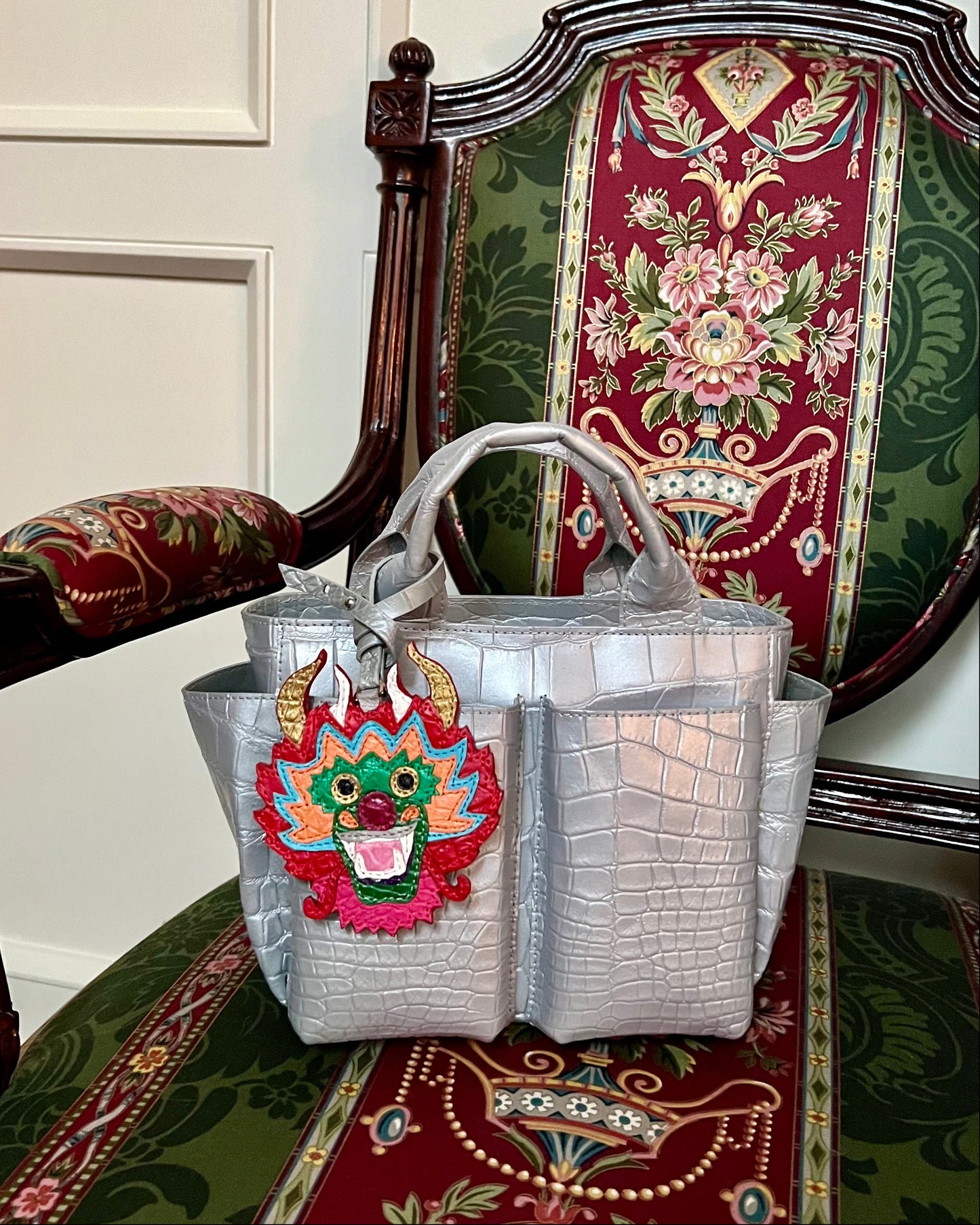 Silver handbag with colorful dragon design on a decorative chair