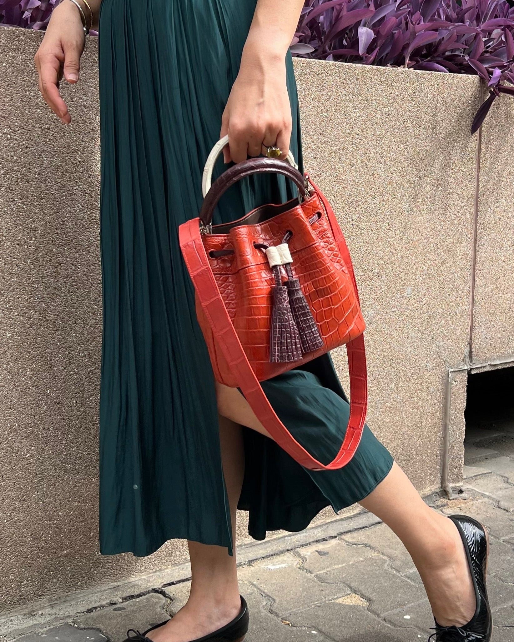 A woman carrying a brick orange top handle bag with three handles.