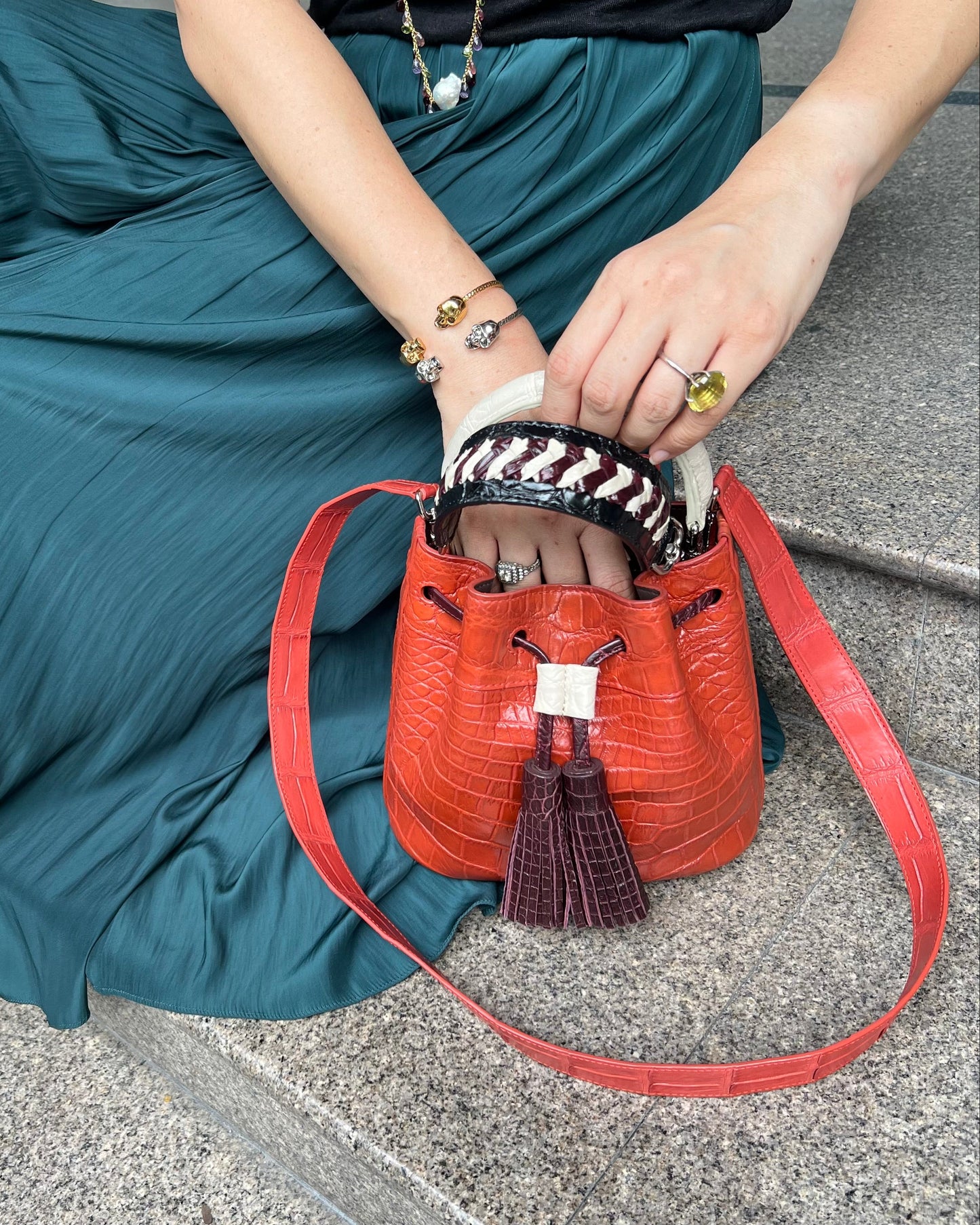 Person holding a red handbag with a patterned strap on a gray pavement.
