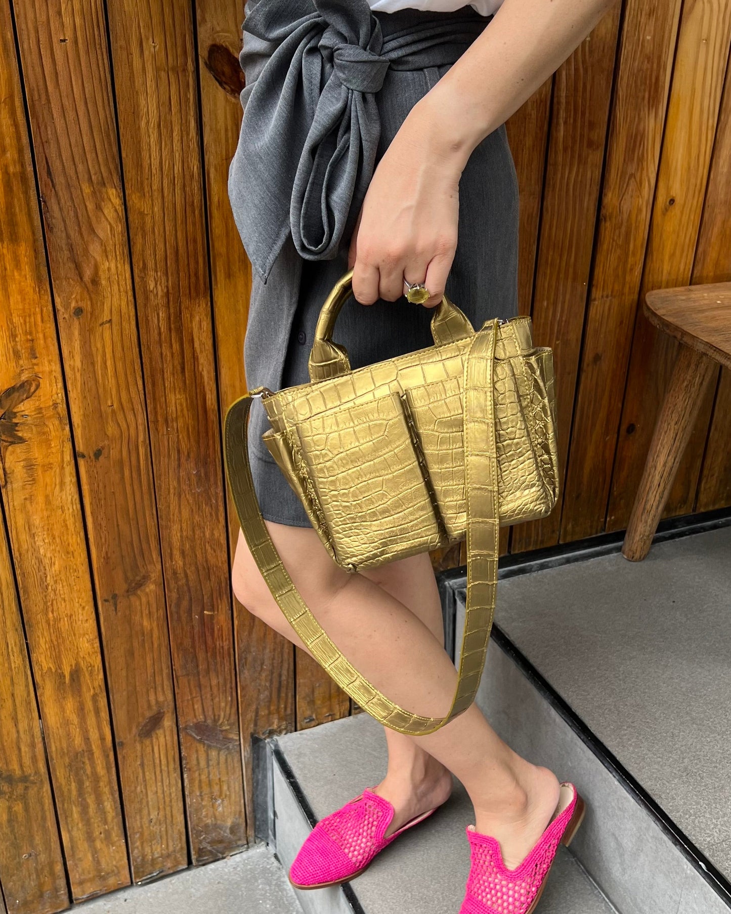 Person holding a gold handbag with pink shoes on a wooden floor.