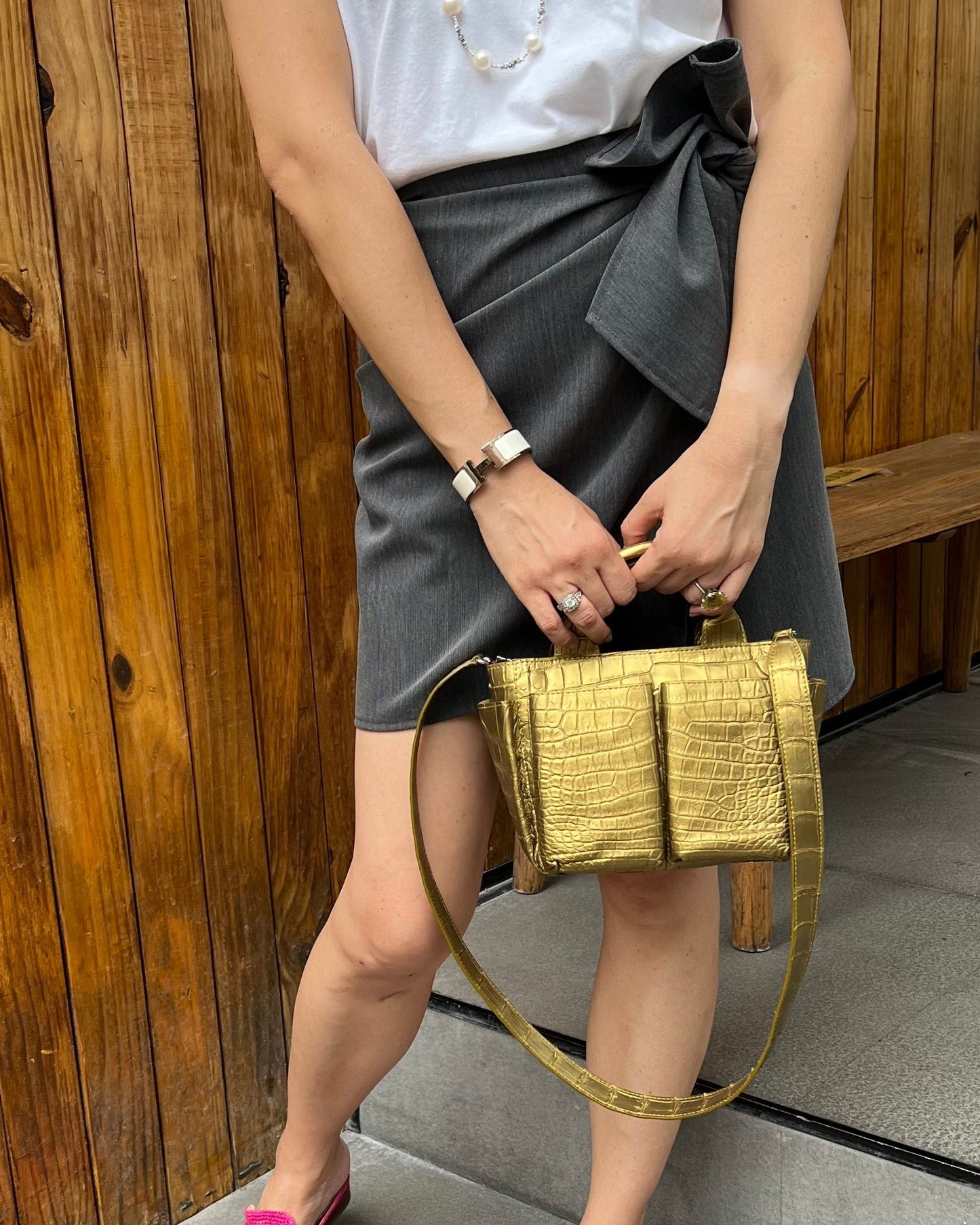Person holding a gold handbag on a wooden and stone surface