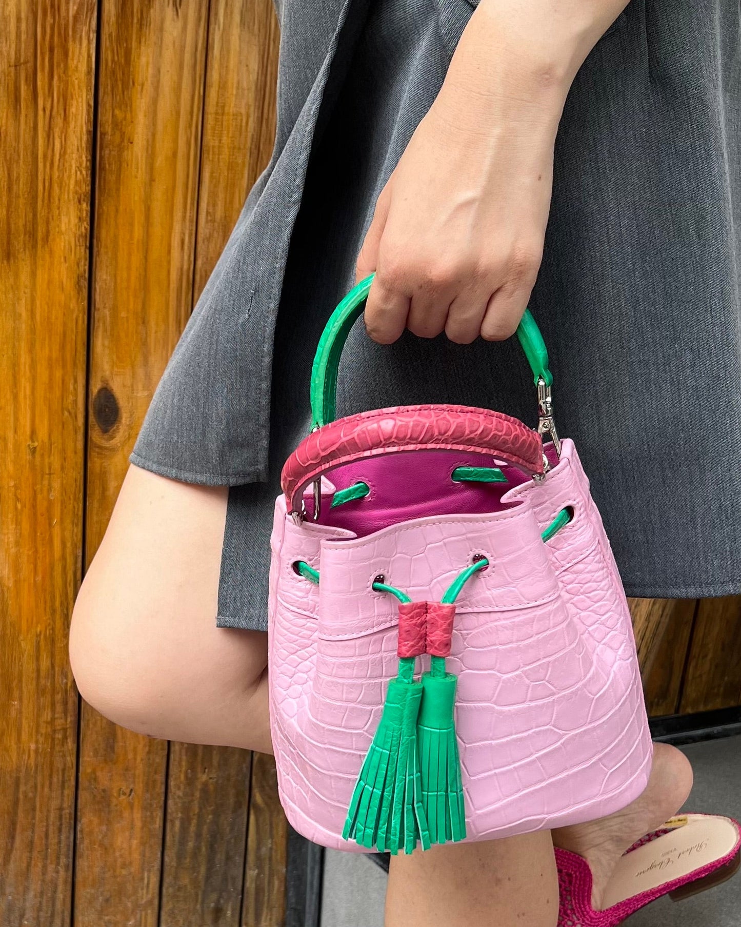 Person holding a pink bucket with green handles and tassels, standing on a wooden deck.