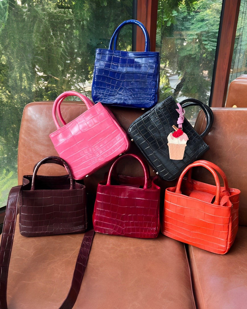 Collection of colorful handbags on a brown leather couch with a glass window in the background.
